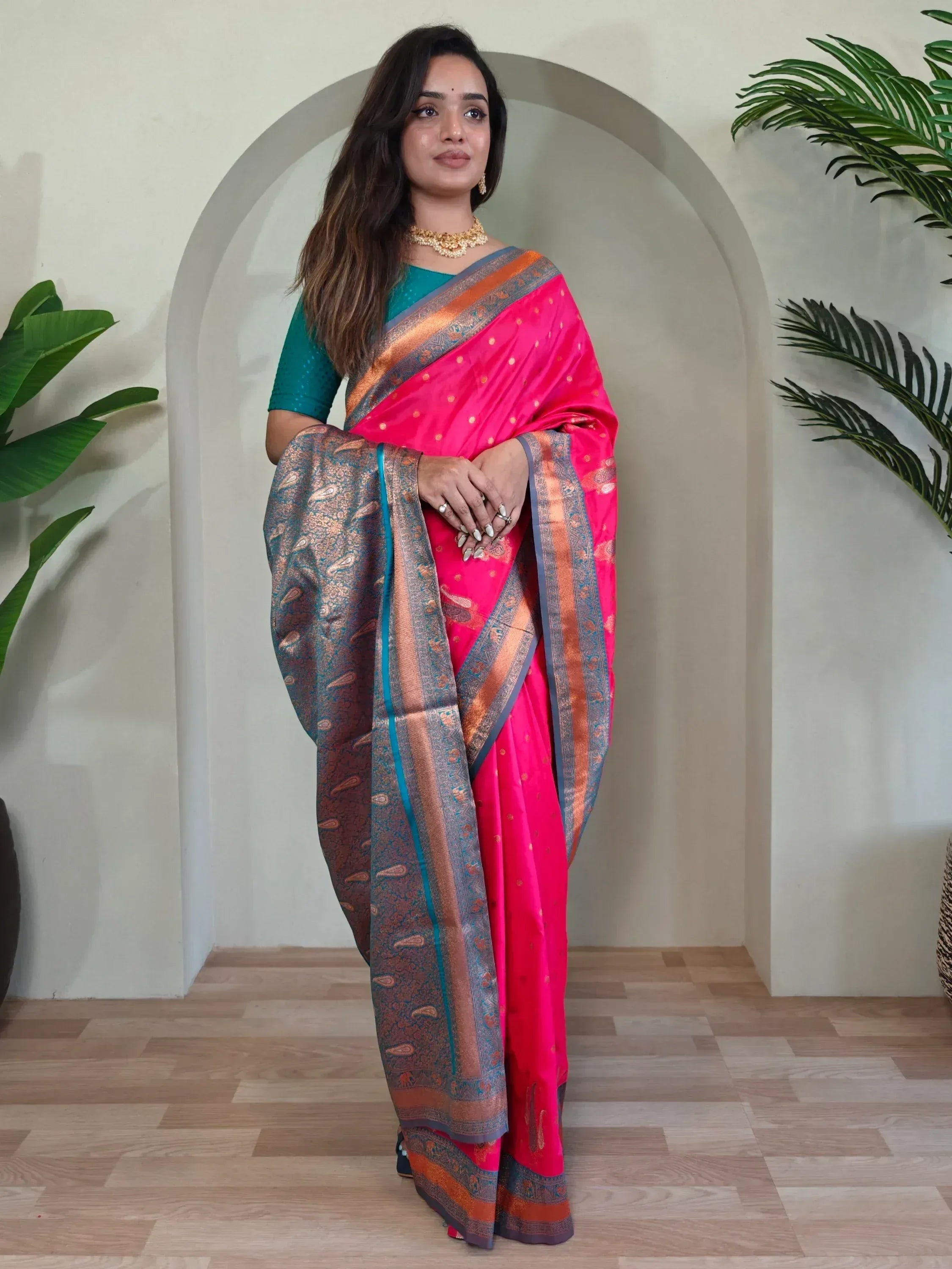 Woman in vibrant pink silk saree with gold paisley border, paired with teal blouse, ideal for Indian ethnic occasions.
