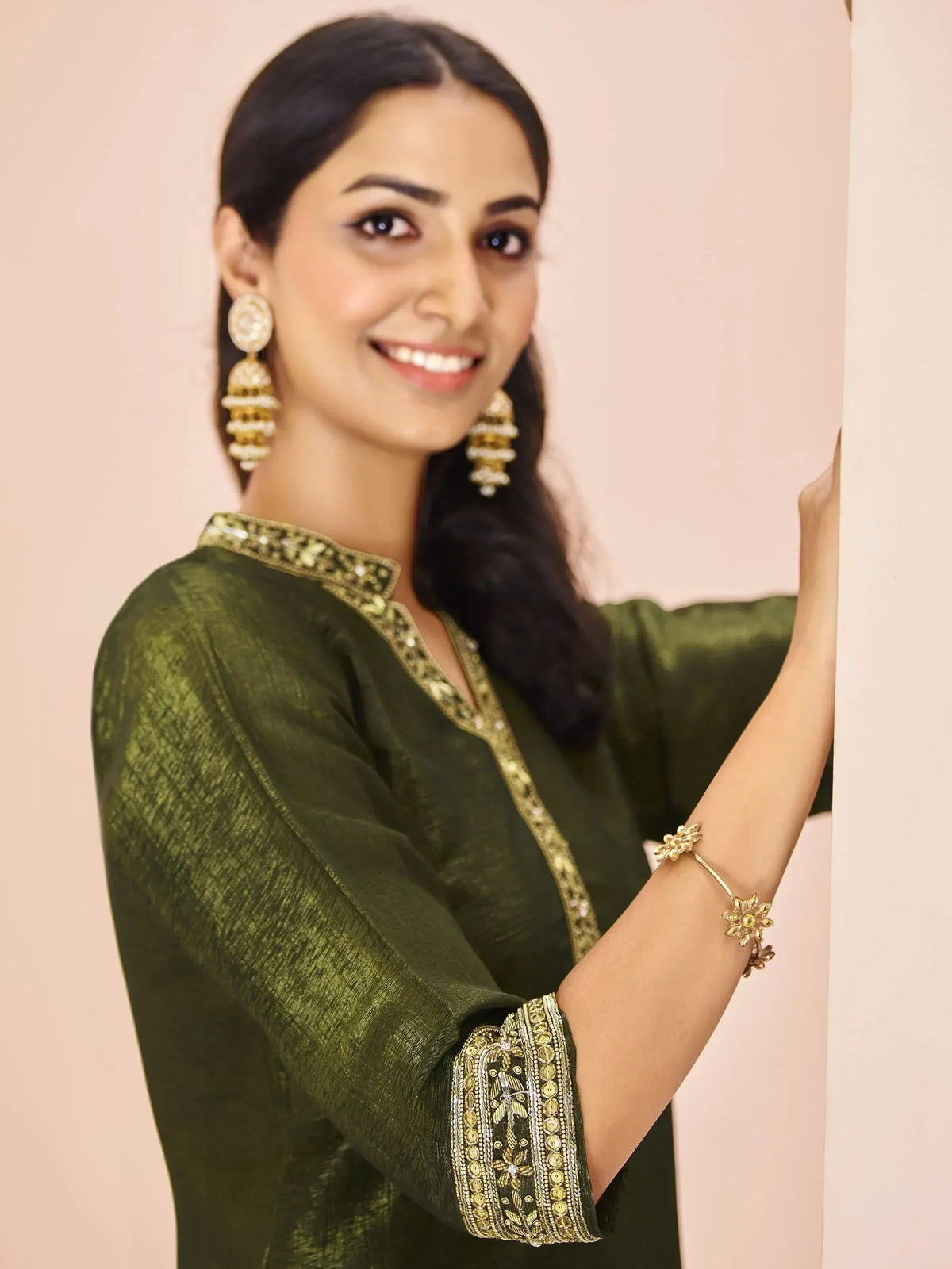 Woman in olive green ethnic kurta with gold embroidery, jhumka earrings, and floral bracelet