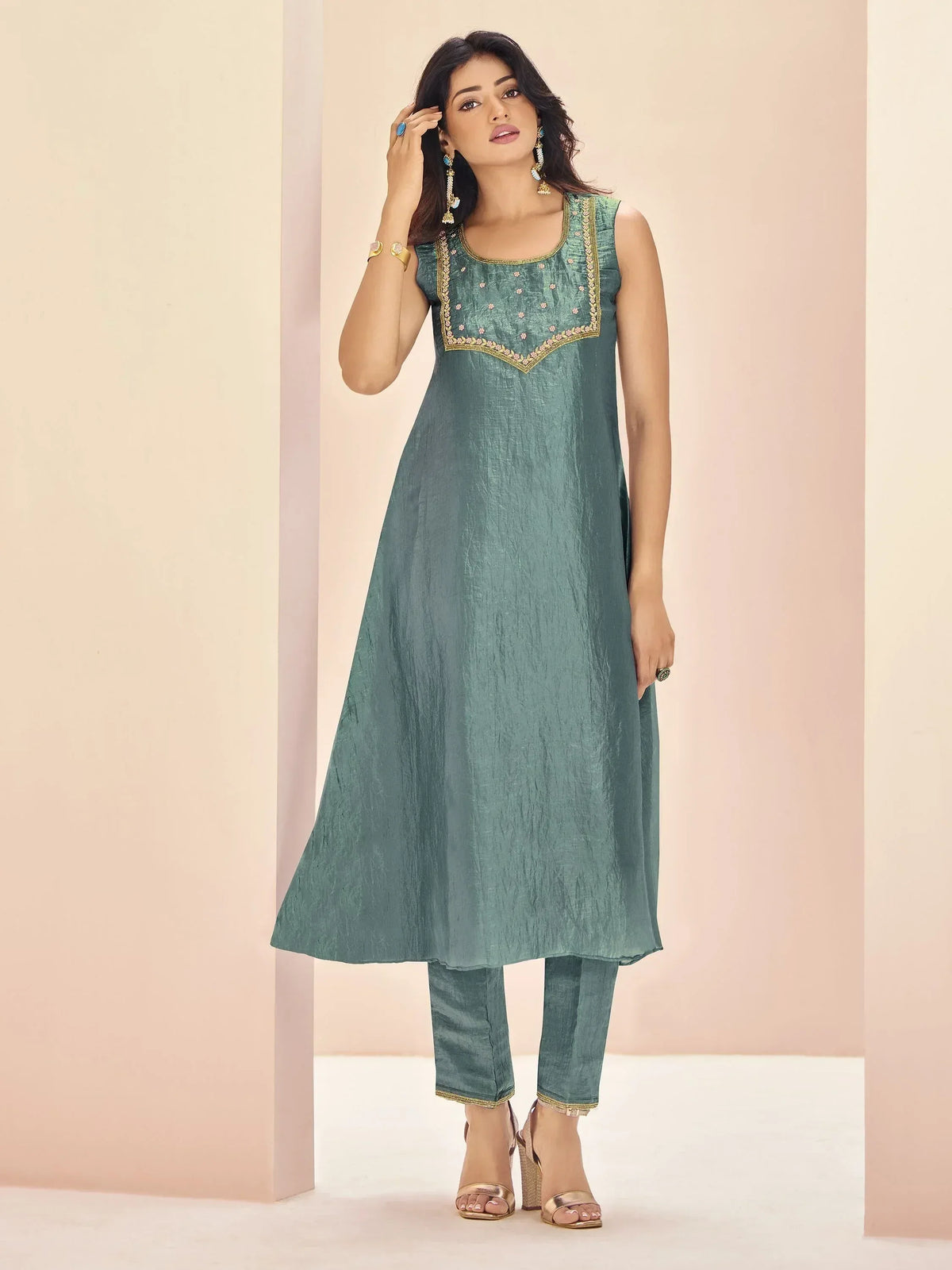 Teal sleeveless ethnic kurta with gold embroidery and matching pants, styled with statement jewelry.