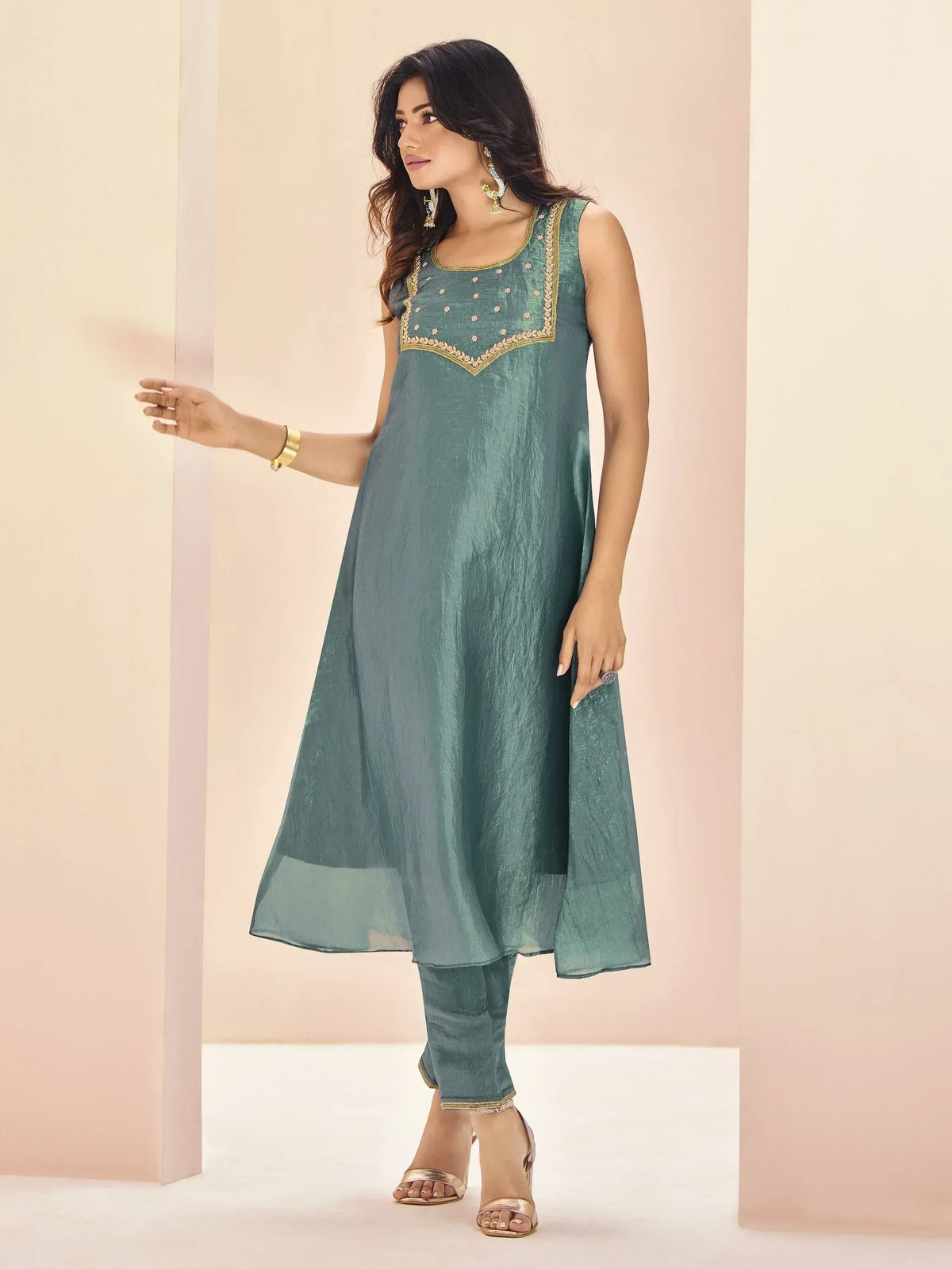 Teal sleeveless ethnic kurta with gold embroidery, paired with matching pants and heels for festive wear.