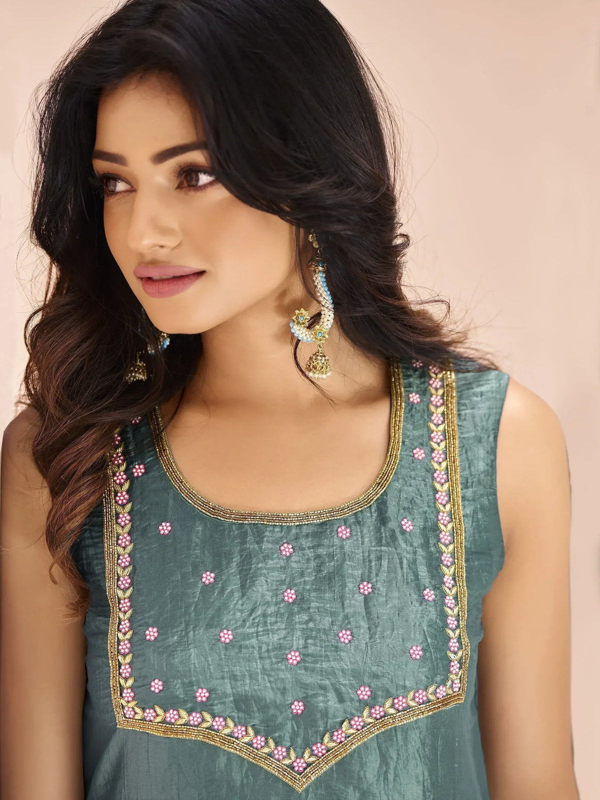 Teal sleeveless ethnic top with pink floral embroidery and gold trim, paired with traditional jhumka earrings