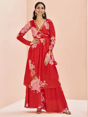 Woman in red floral ethnic gown with long sleeves, standing against a pastel background