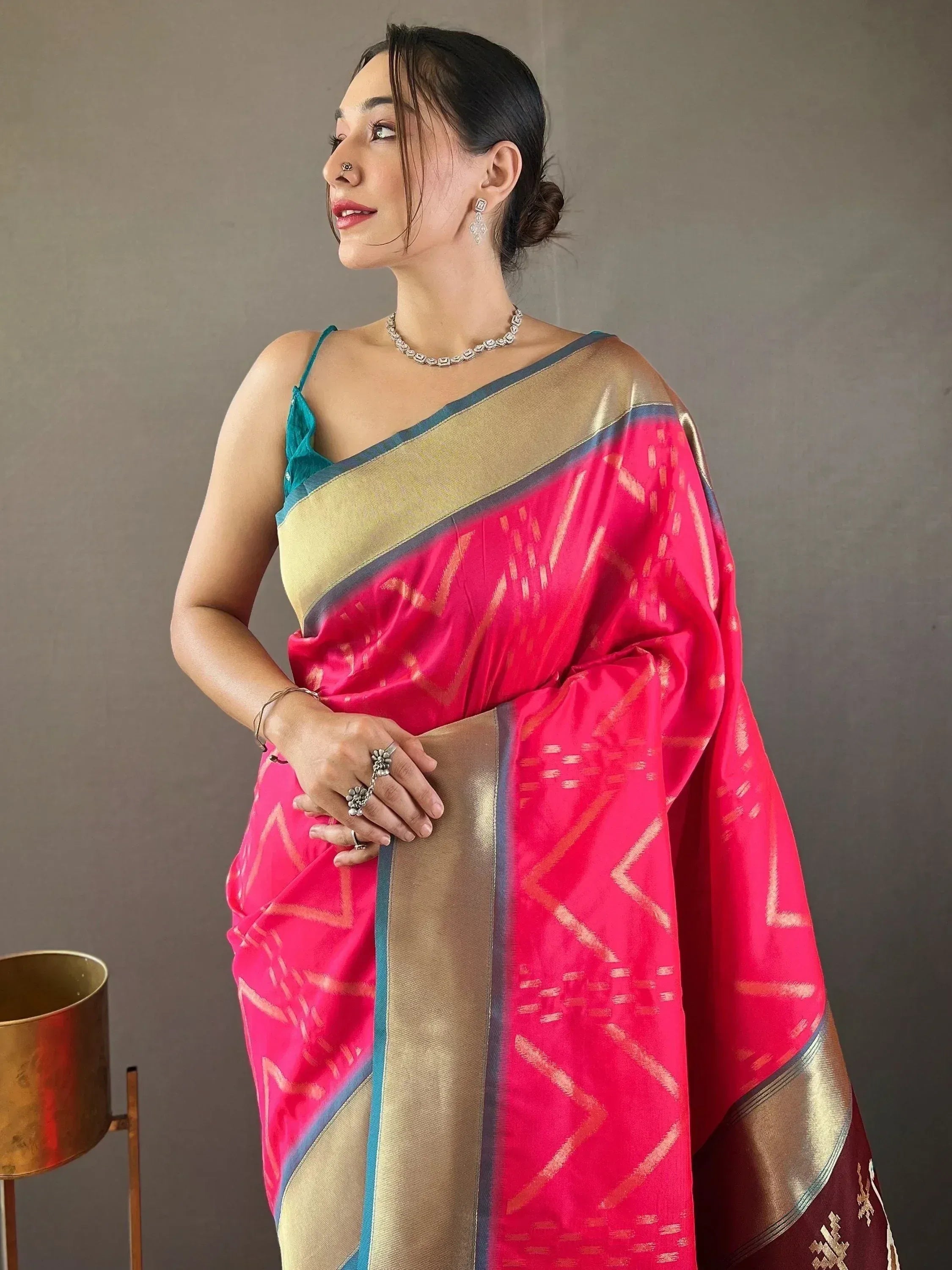 Woman in vibrant pink and gold ethnic saree with geometric patterns, paired with teal blouse and jewelry