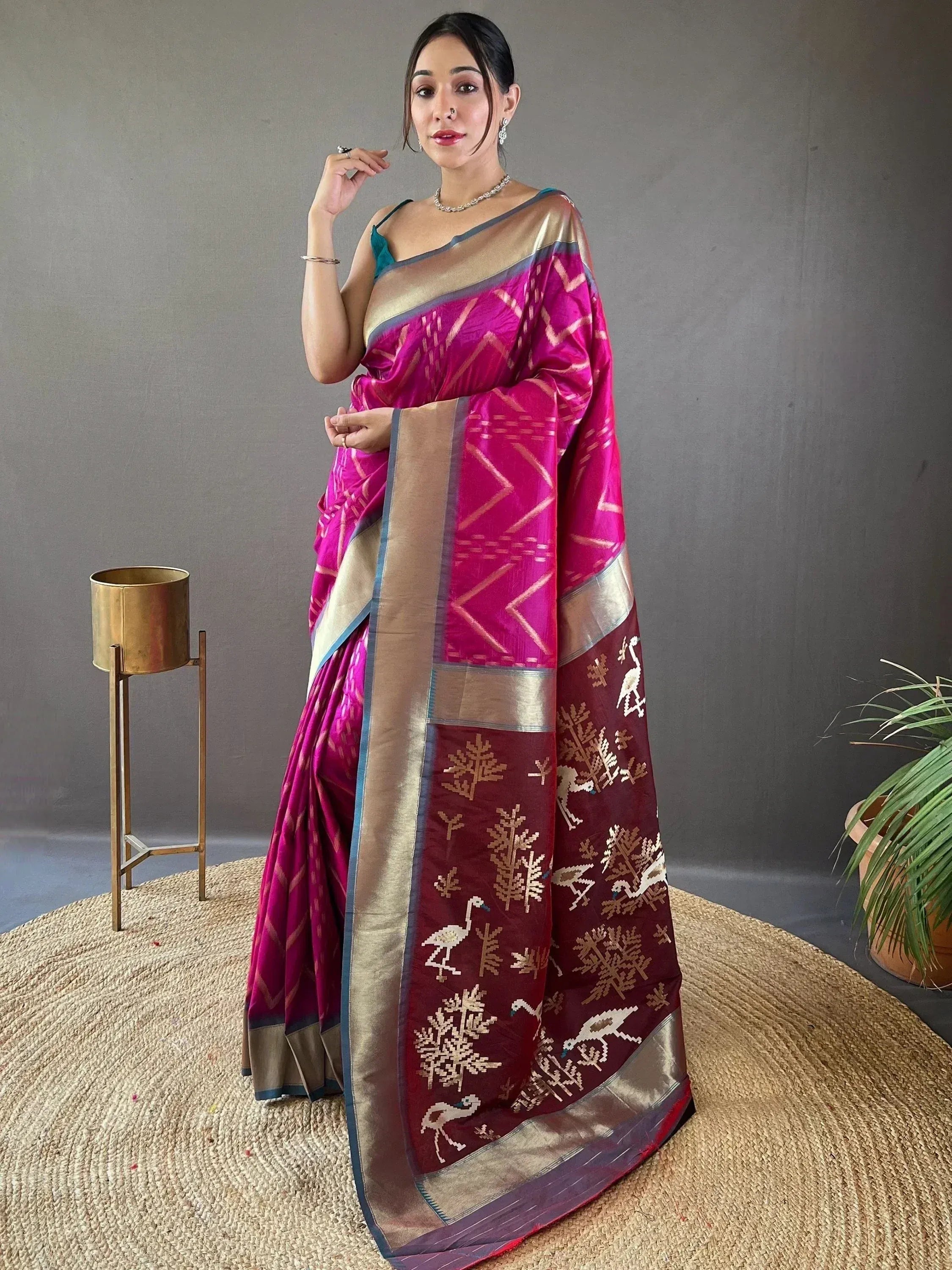 Woman in vibrant pink and maroon ethnic saree with bird and tree motifs, gold border, styled for festive occasions