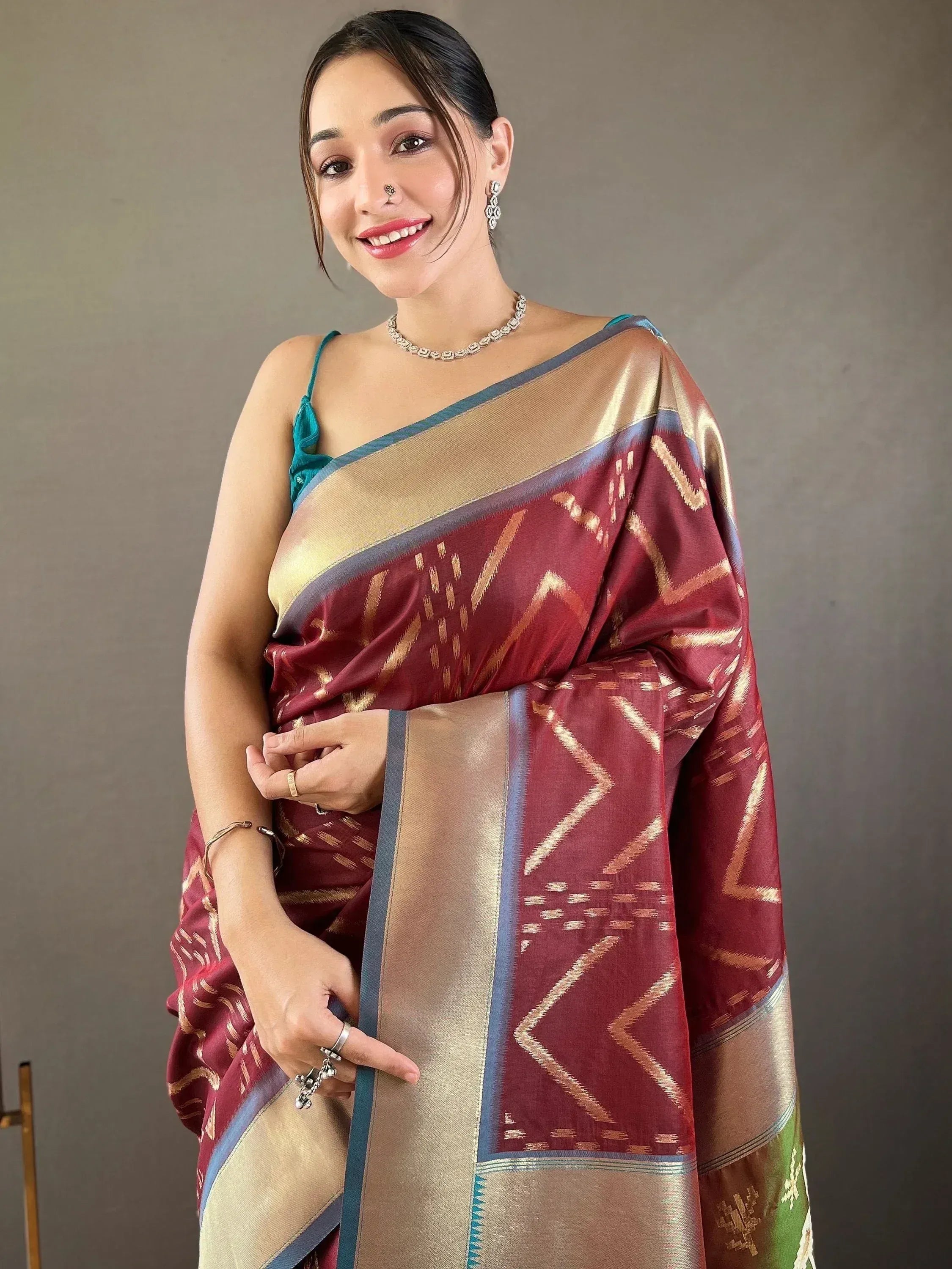 Woman in maroon and gold ethnic saree with geometric patterns, paired with teal blouse and jewelry