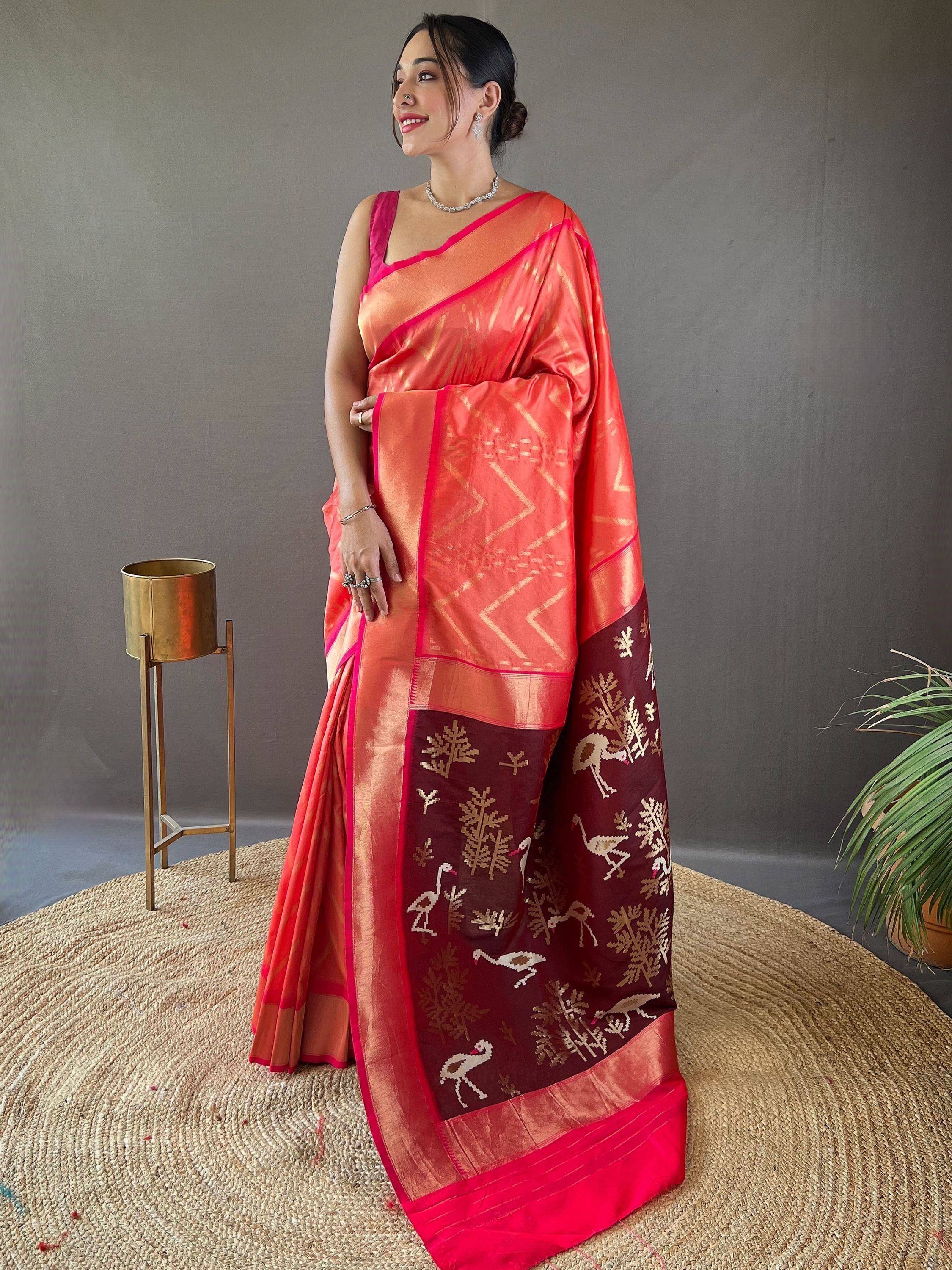 Woman in vibrant coral saree with maroon border featuring bird and tree motifs, styled for ethnic occasions
