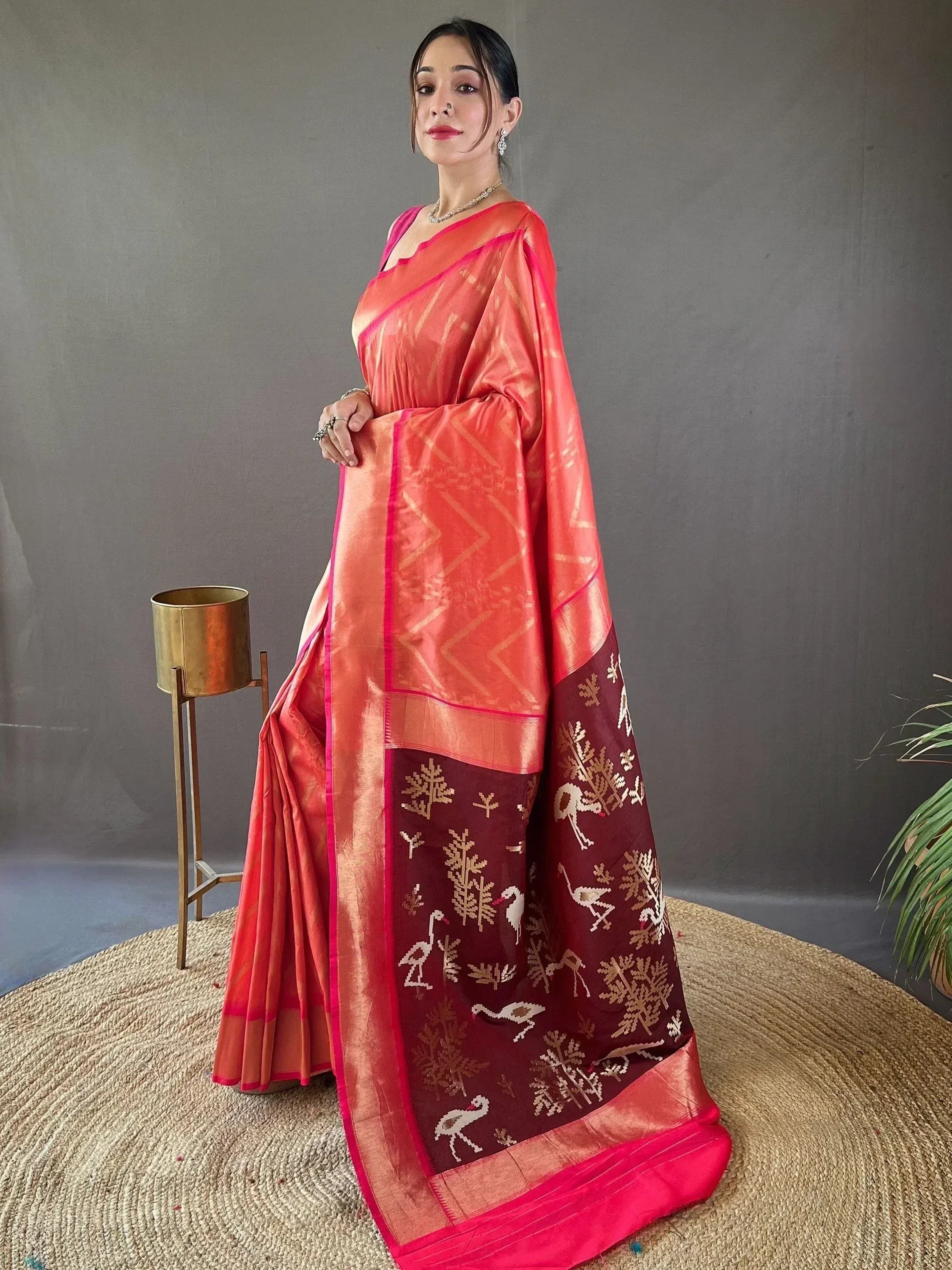 Woman in coral pink saree with maroon border featuring bird and tree motifs, Indian ethnic wear