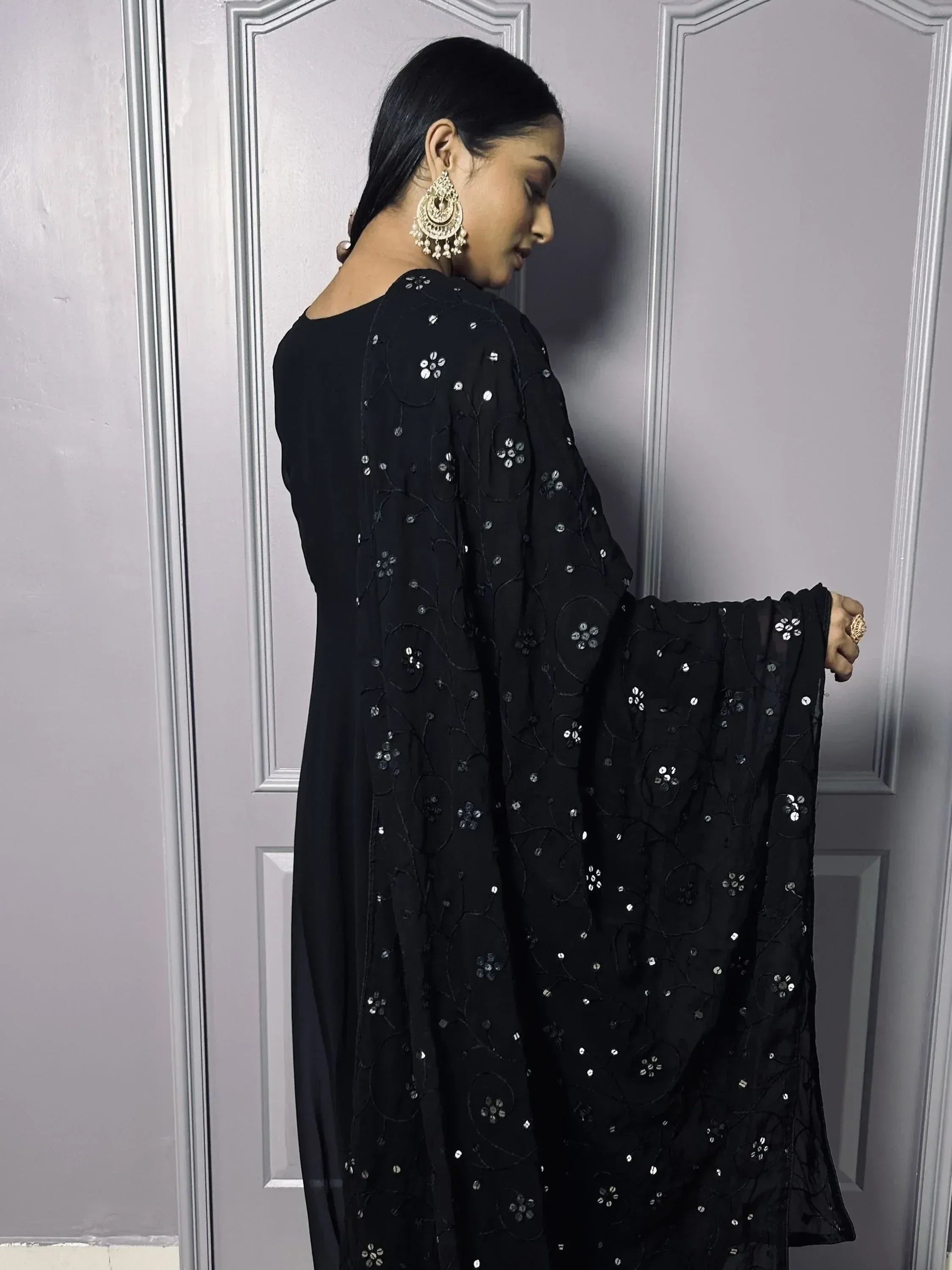 Woman in black embroidered ethnic gown with sequins, statement earrings, and dupatta