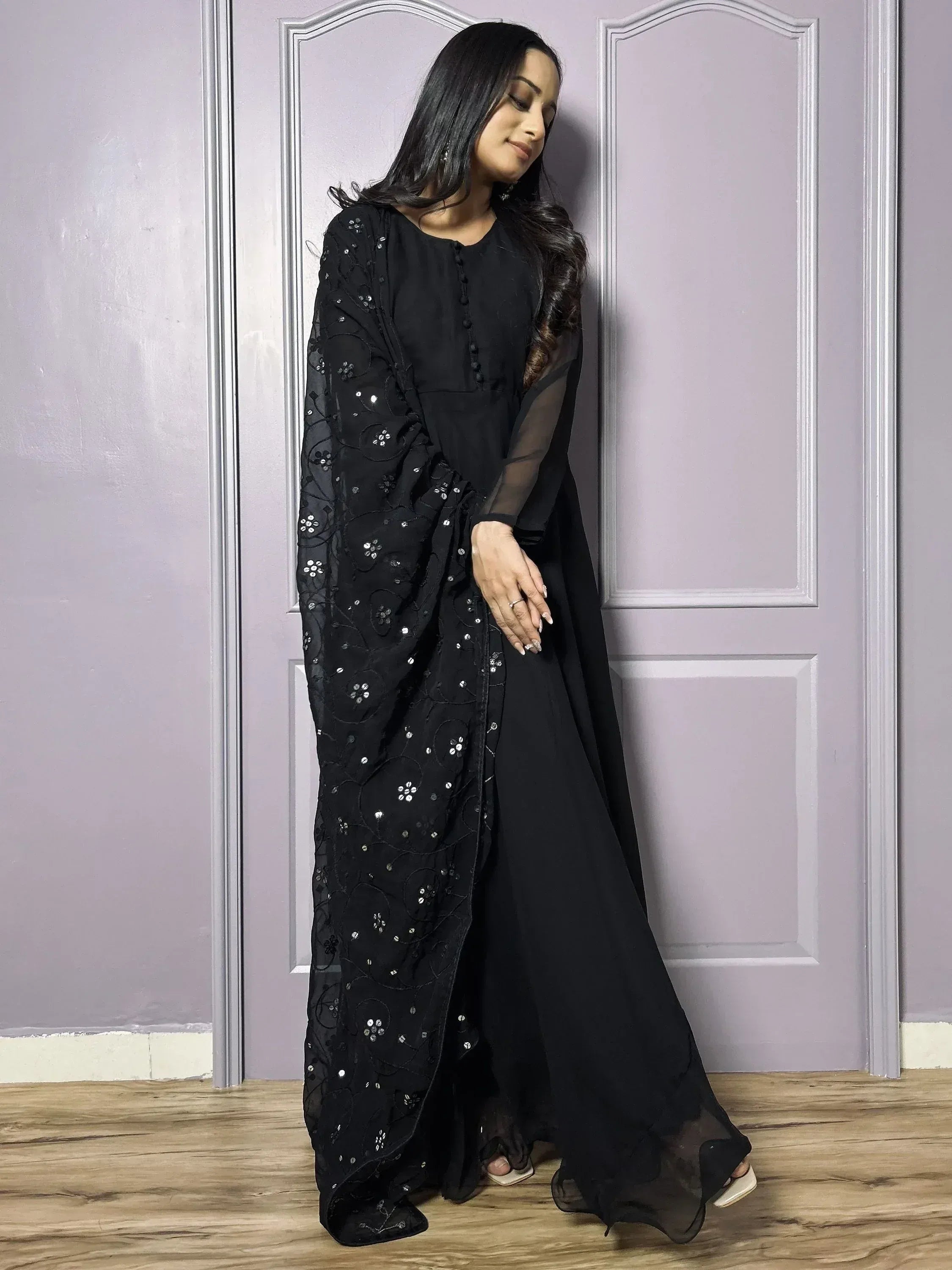 Woman in black embroidered ethnic gown with sheer dupatta, standing indoors