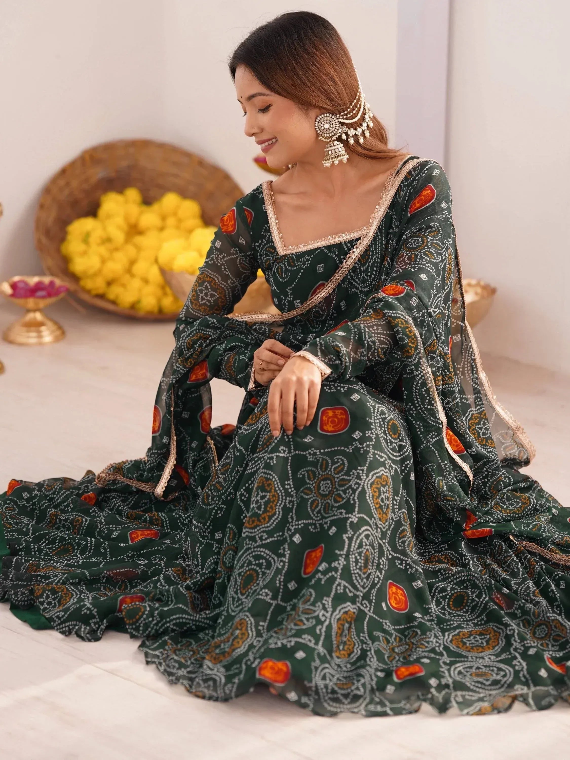 Elegant green printed ethnic gown with intricate patterns and gold trim, paired with traditional jewelry.