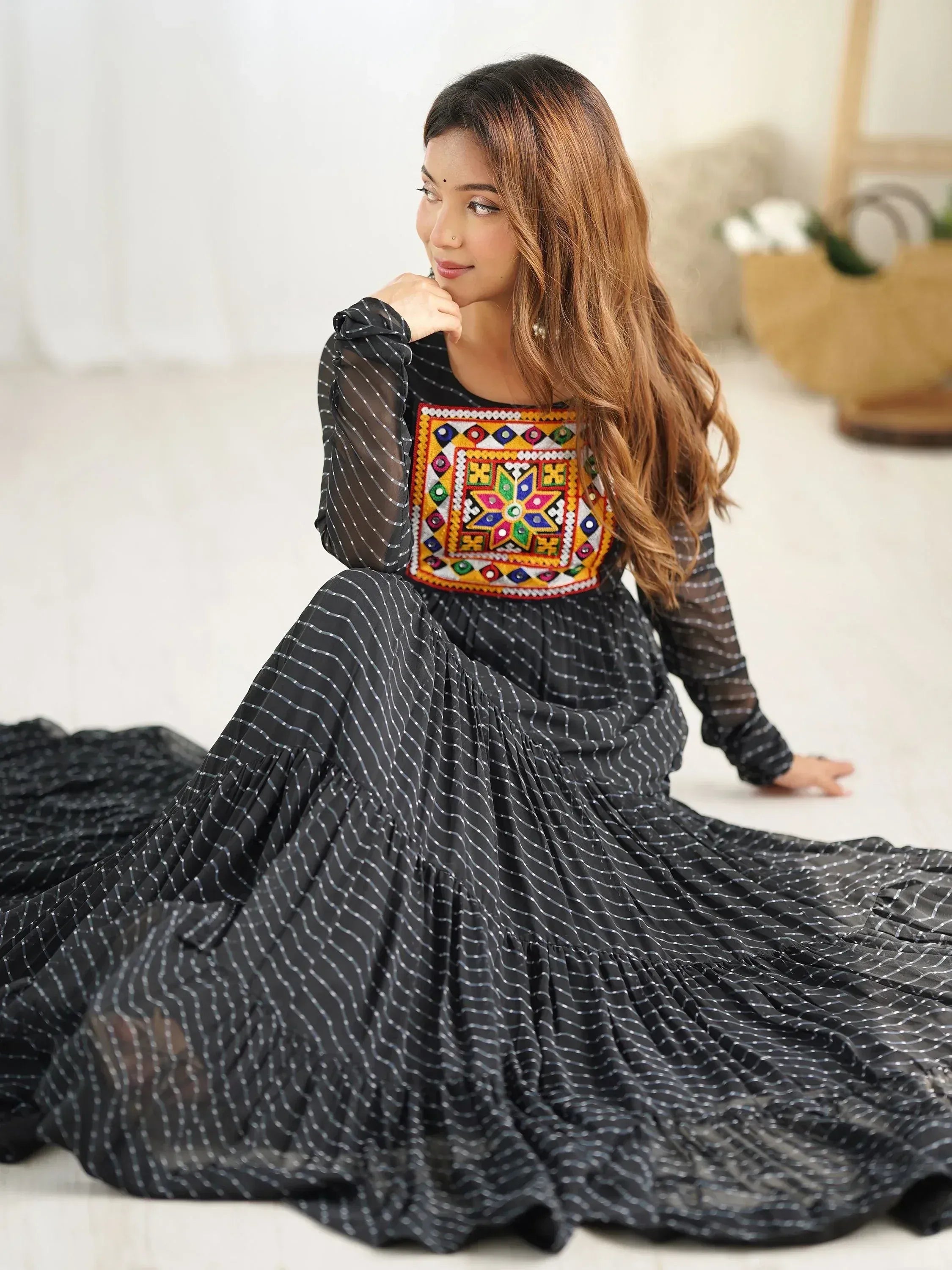 Woman in black ethnic gown with mirror work embroidery and white stripes sitting indoors