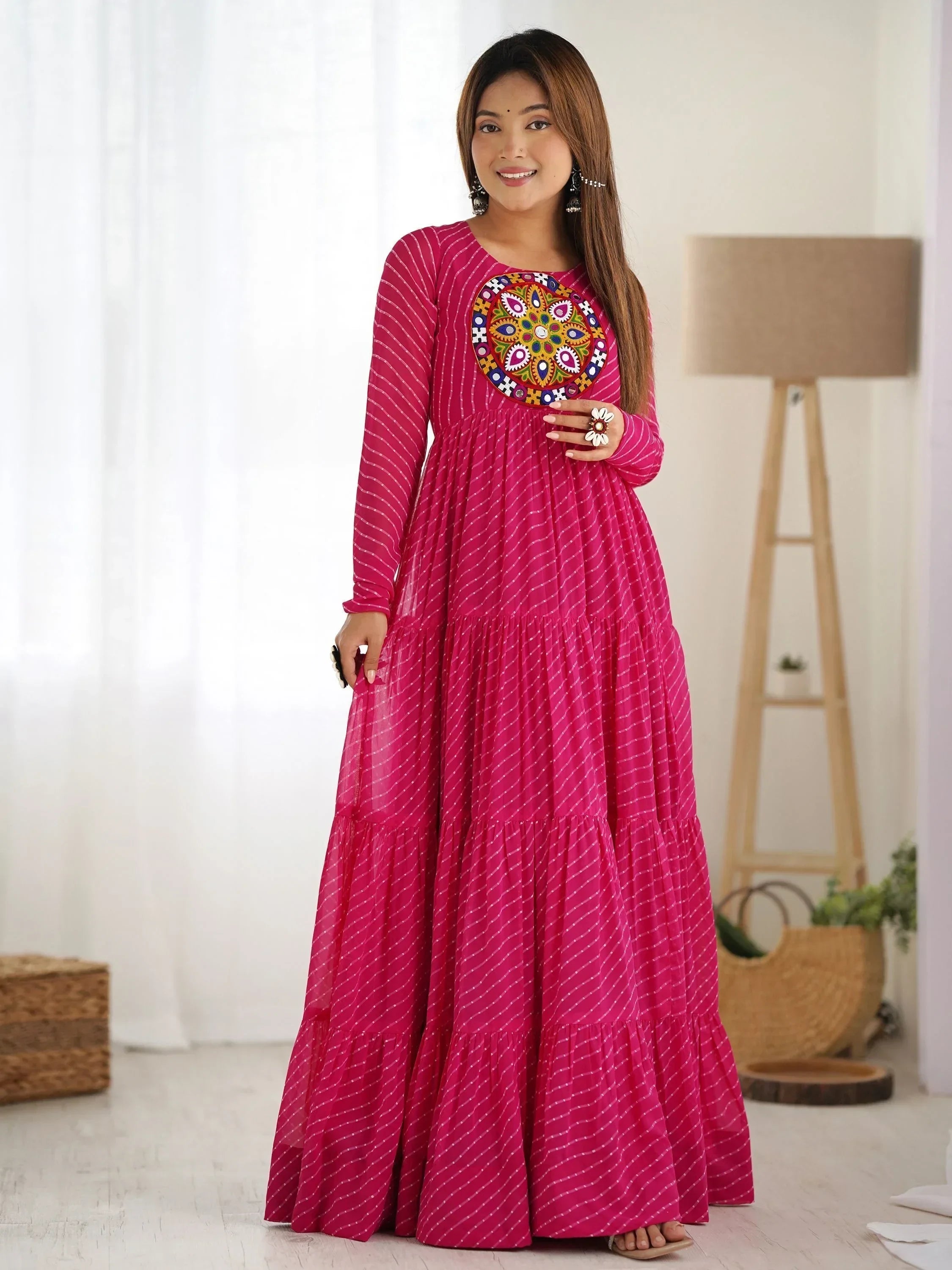 Woman in a pink ethnic gown with mirror work embroidery and long sleeves, standing indoors