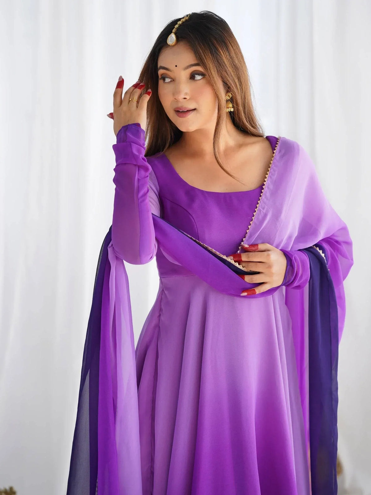Purple ethnic gown with sheer dupatta, gold trim, and traditional jewelry for Indian wear