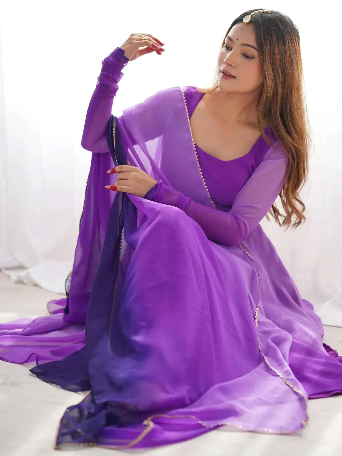 Purple ethnic gown with sheer sleeves and gold trim, styled with maang tikka for Indian occasions