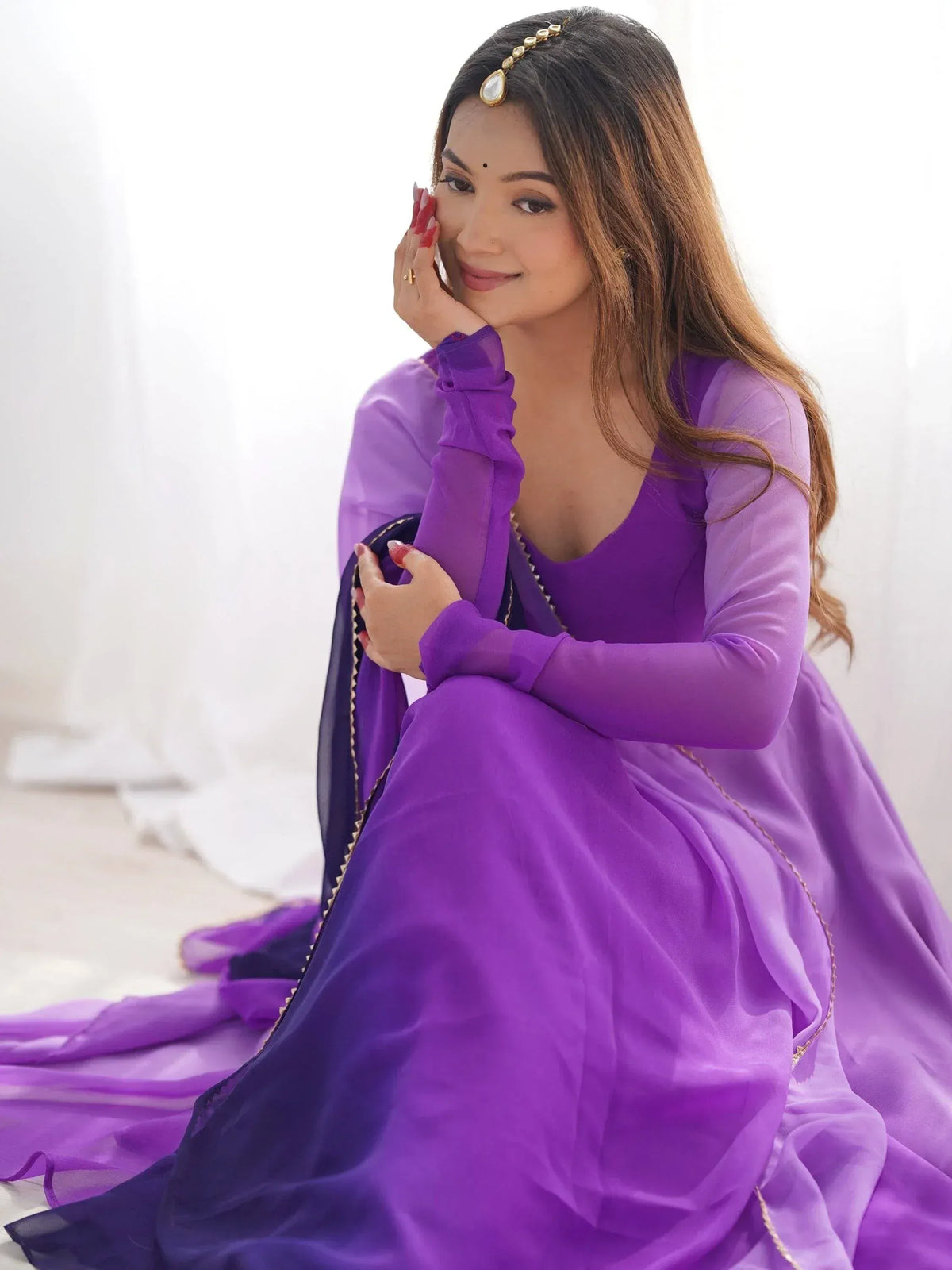Woman in purple ethnic gown with sheer sleeves and gold trim, wearing maang tikka, ideal for Indian occasions