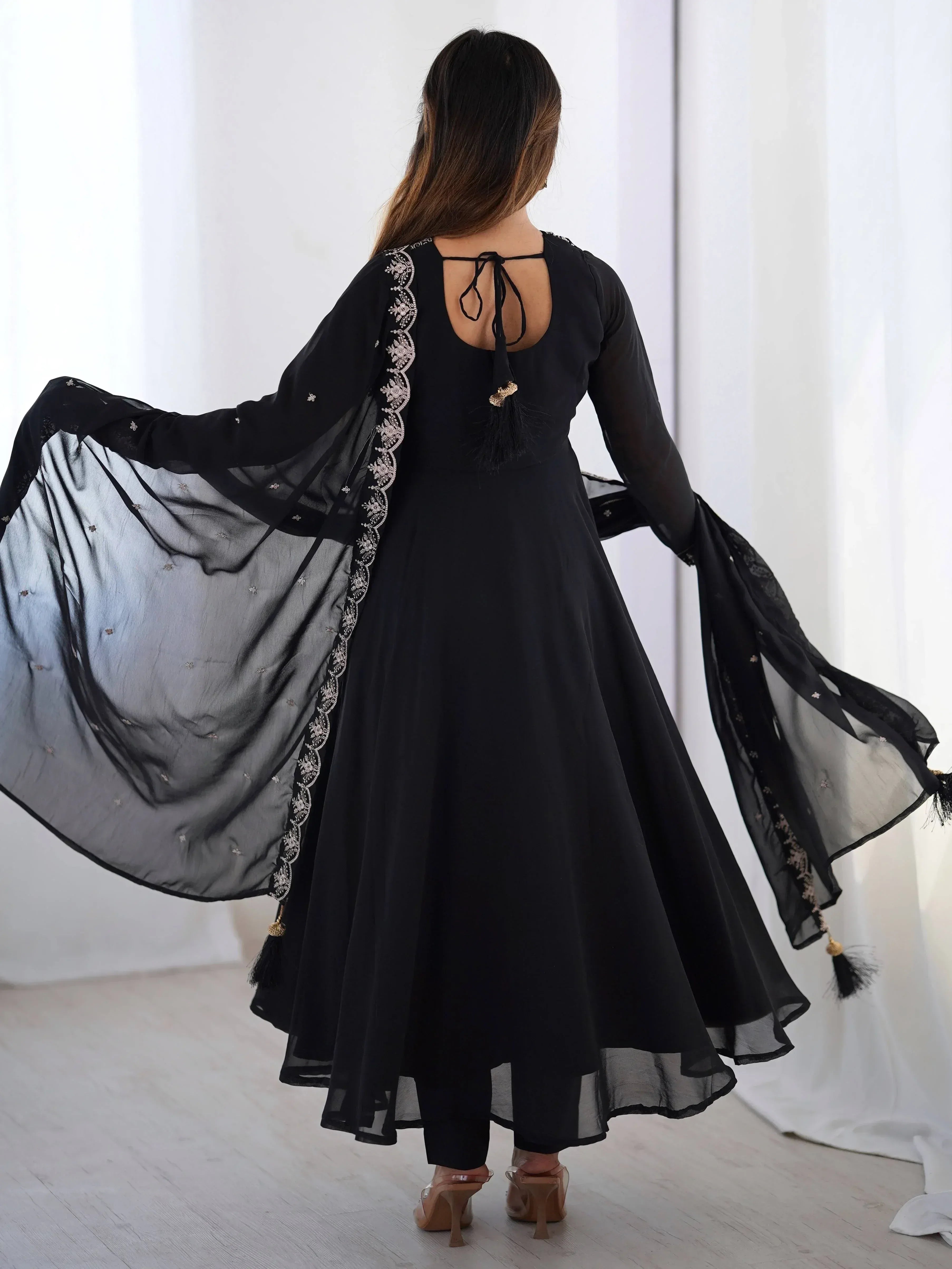 Black ethnic anarkali suit with sheer embroidered dupatta, back view showing tie-up detail and tassels.