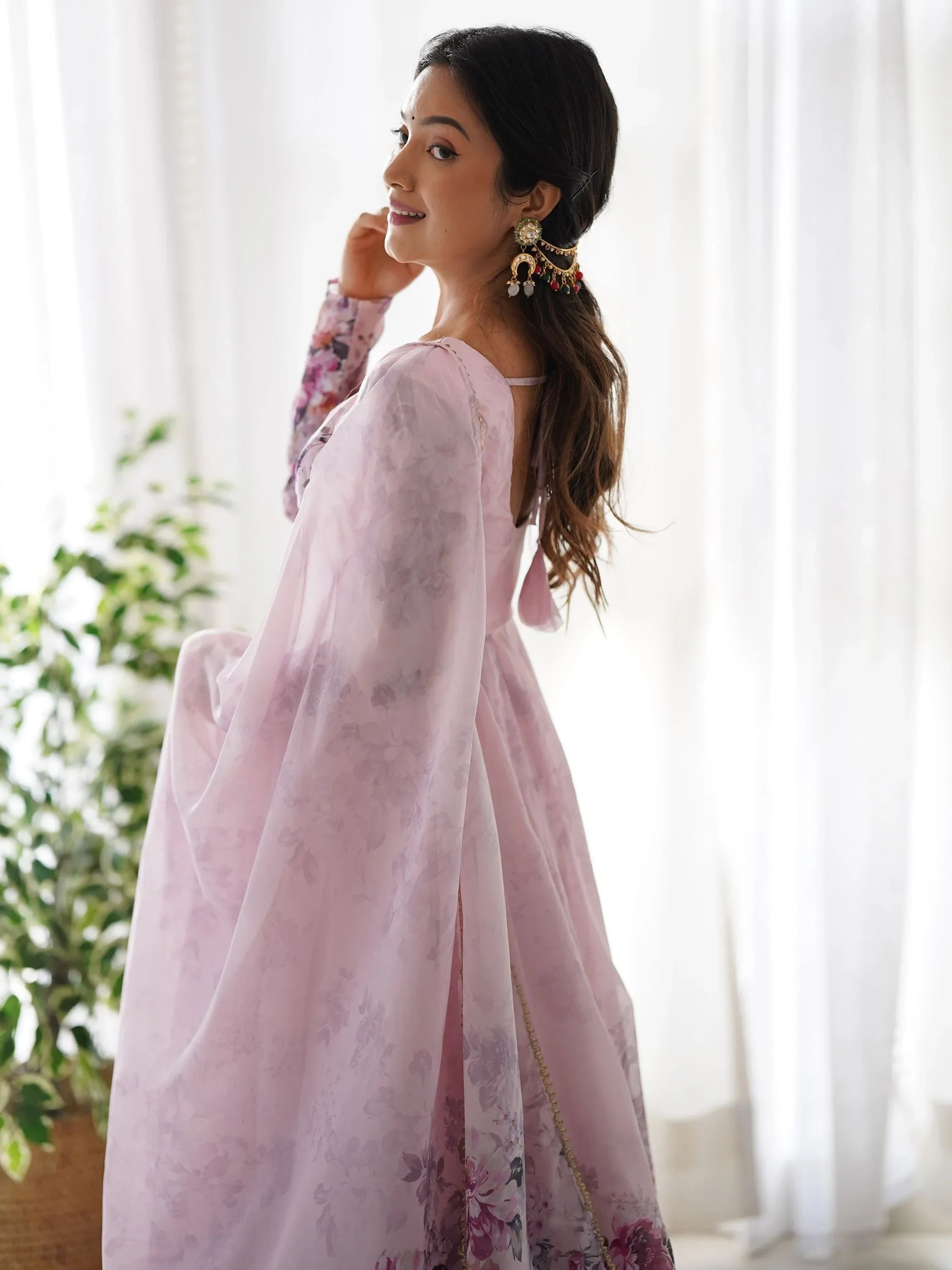 Woman in pastel pink floral saree with statement earrings, standing by a window