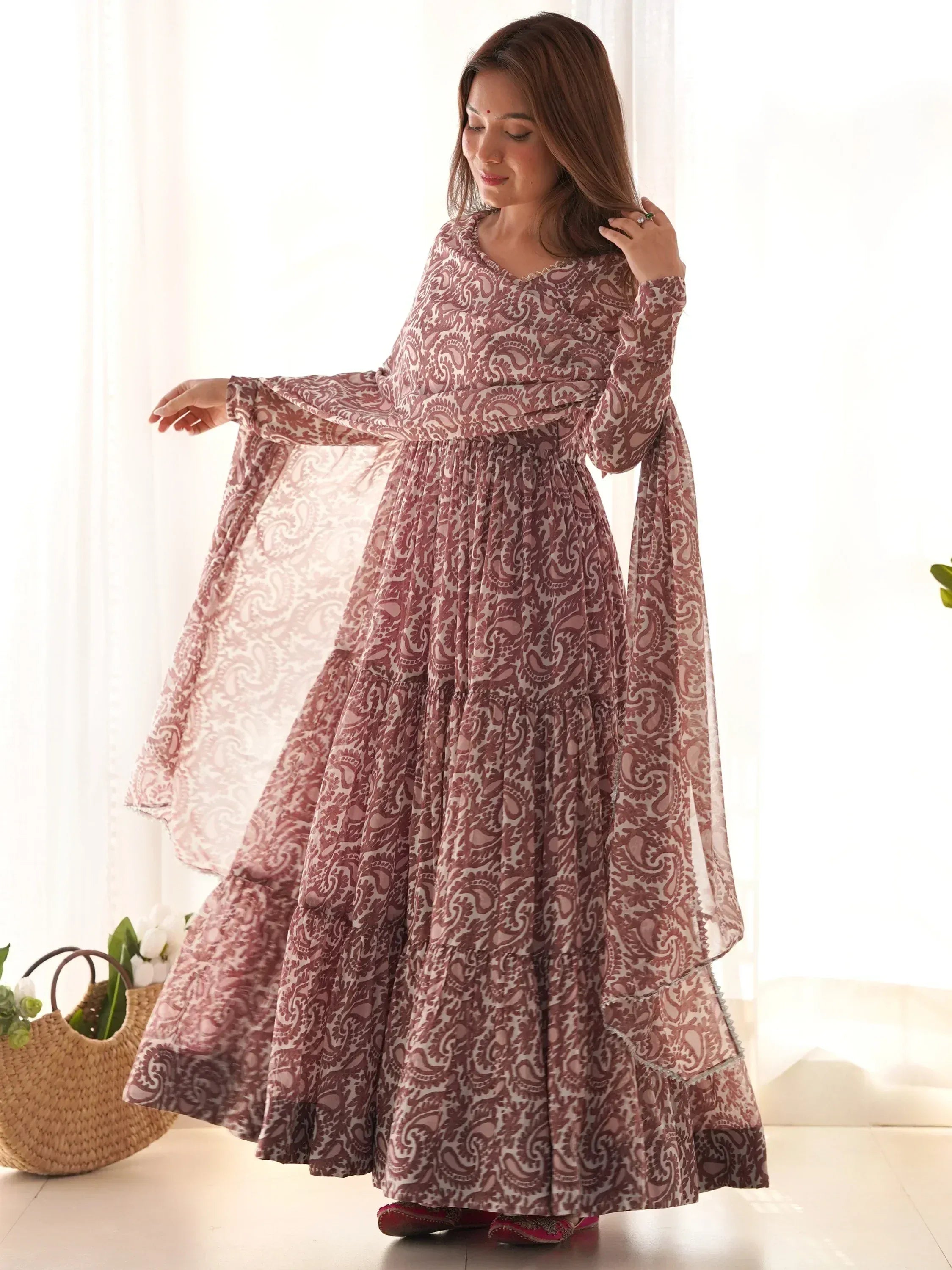 Woman in printed maroon ethnic gown with full sleeves and flare, standing indoors