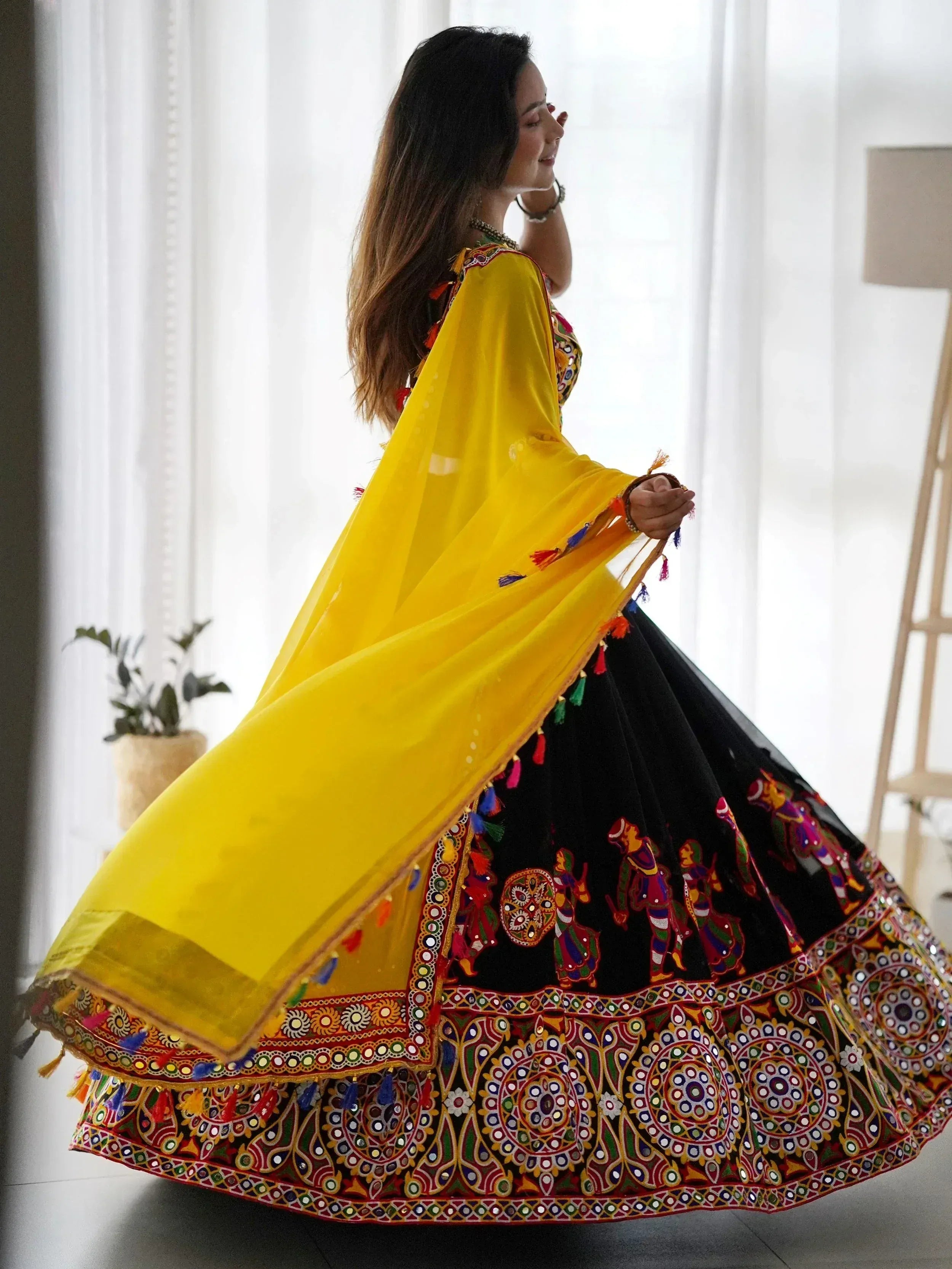 Woman in vibrant yellow and black ethnic lehenga with mirror work and tassels, perfect for Indian celebrations.