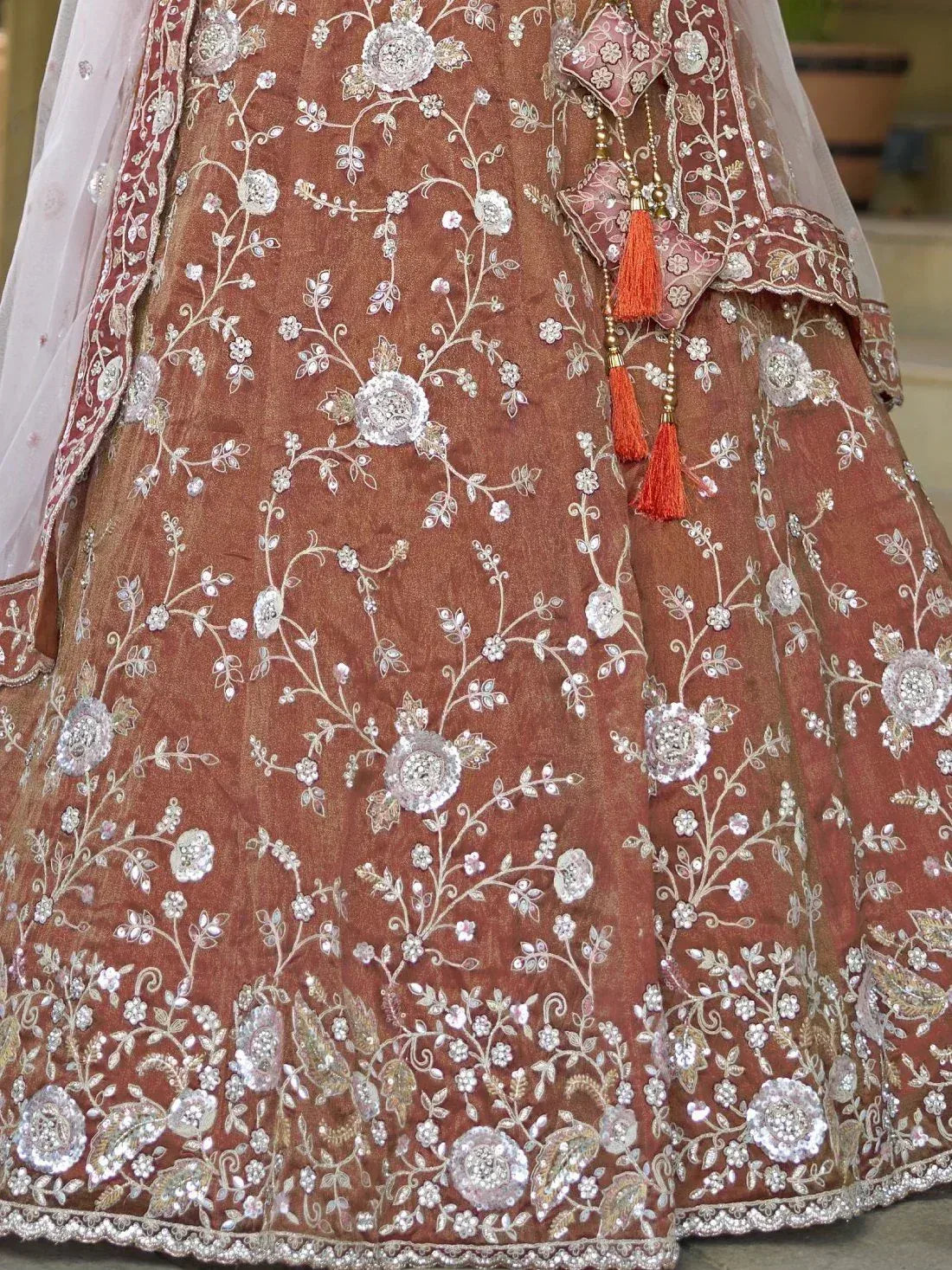 Brown designer lehenga with silver floral embroidery and orange tassels, perfect for Indian weddings