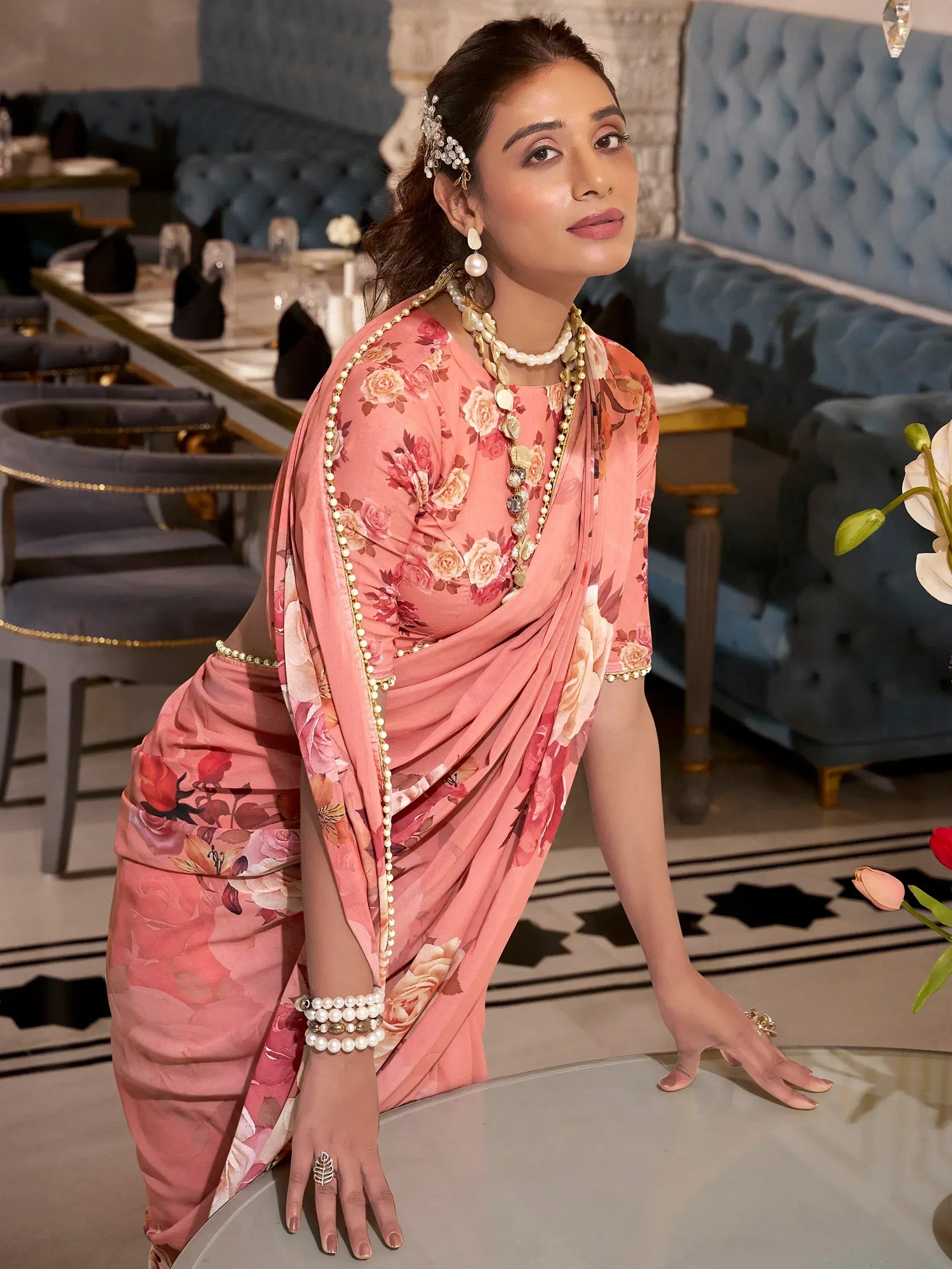 Elegant woman in floral pink saree with pearl jewelry, styled for Indian ethnic wear occasions.
