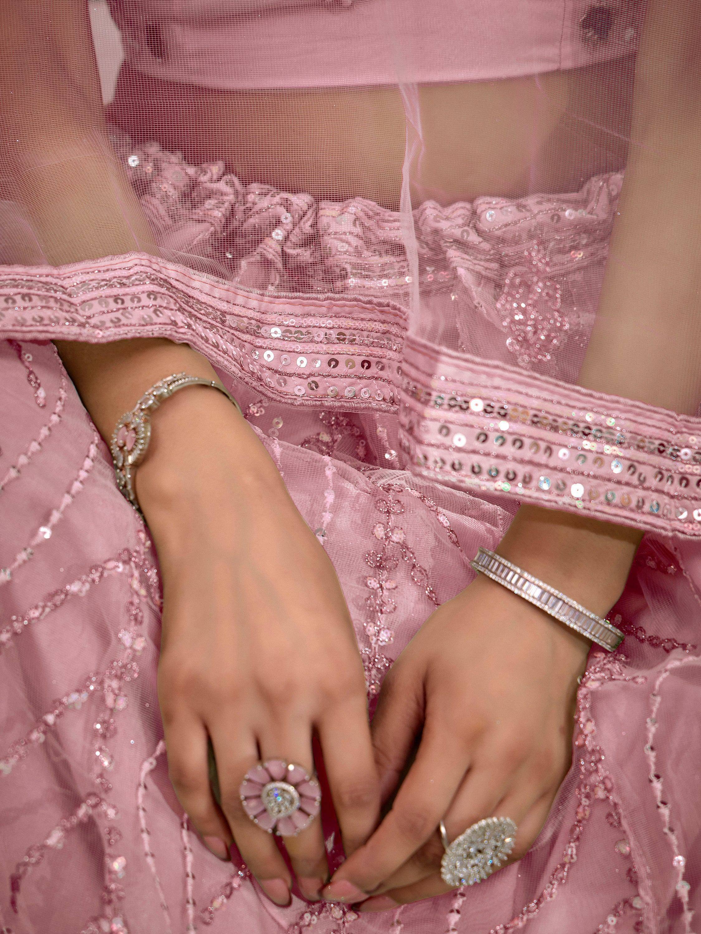 Pink sequin lehenga choli with sheer overlay, statement rings, and diamond bracelets for Indian ethnic wear