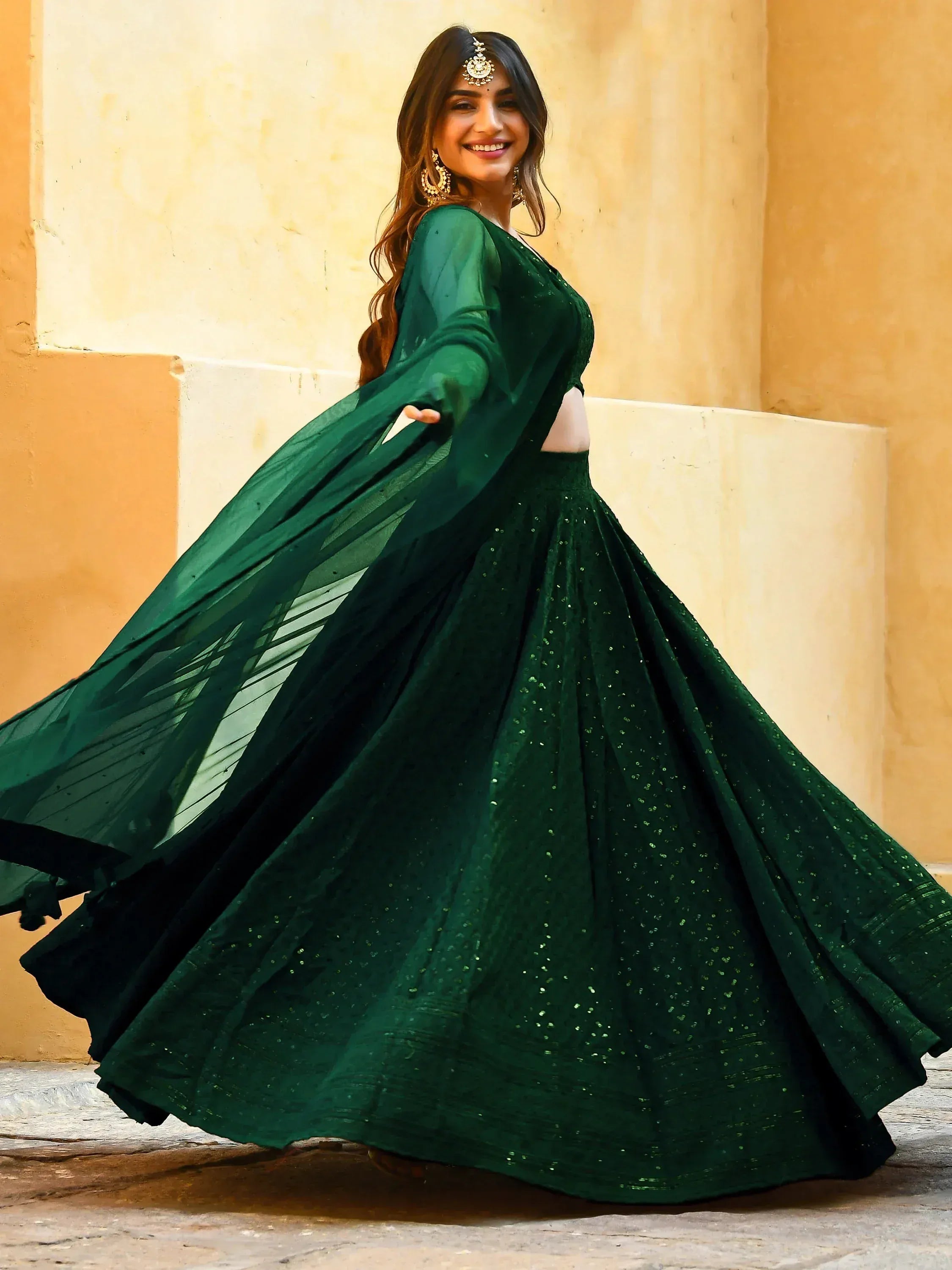 Emerald green designer lehenga choli with sequins, sheer sleeves, and traditional jewelry for Indian ethnic wear.