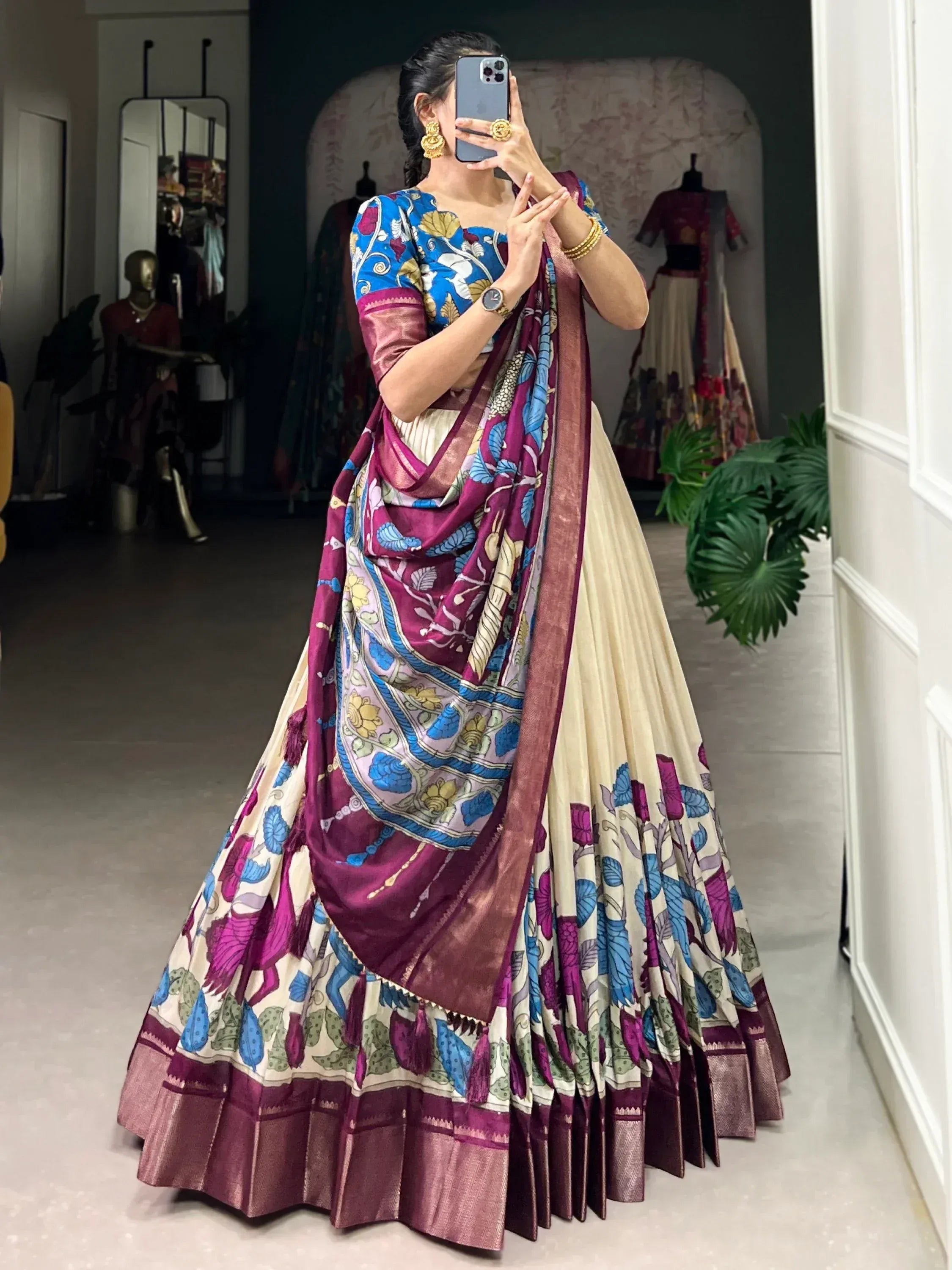 Woman in vibrant floral lehenga choli with purple and blue dupatta, taking mirror selfie in boutique