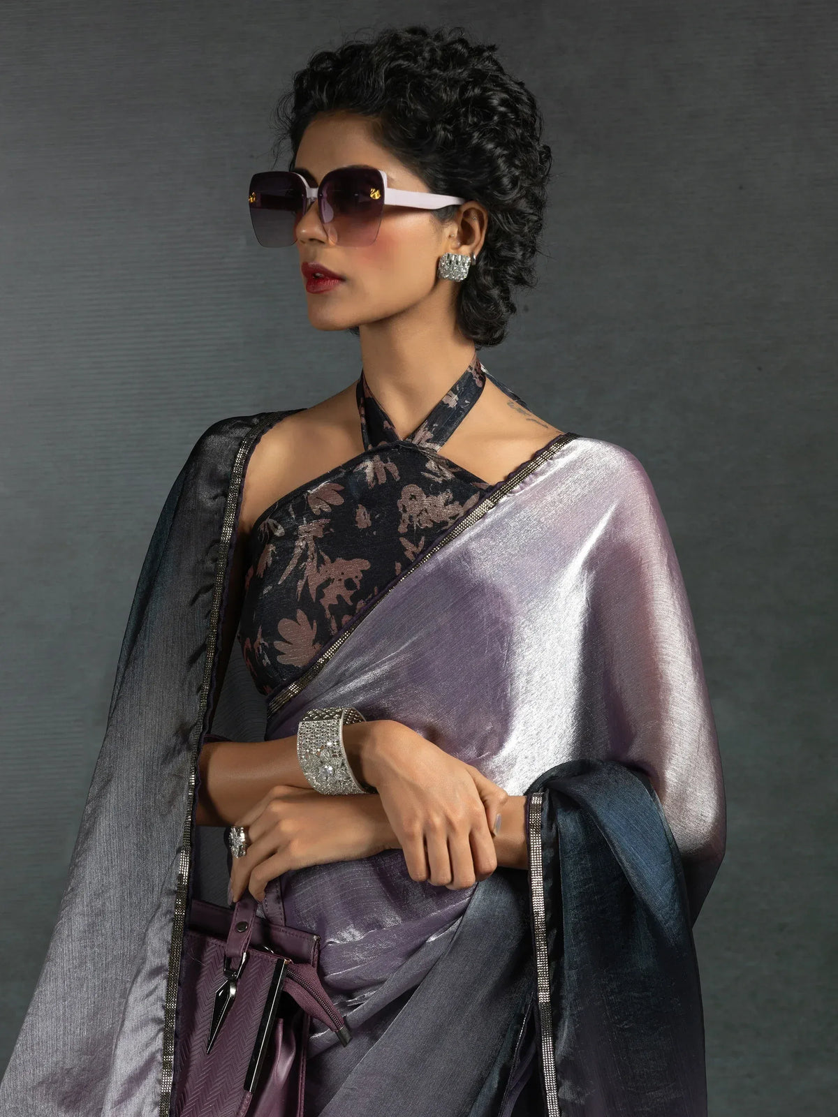 Stylish woman in purple metallic saree with floral blouse, sunglasses, and statement jewelry