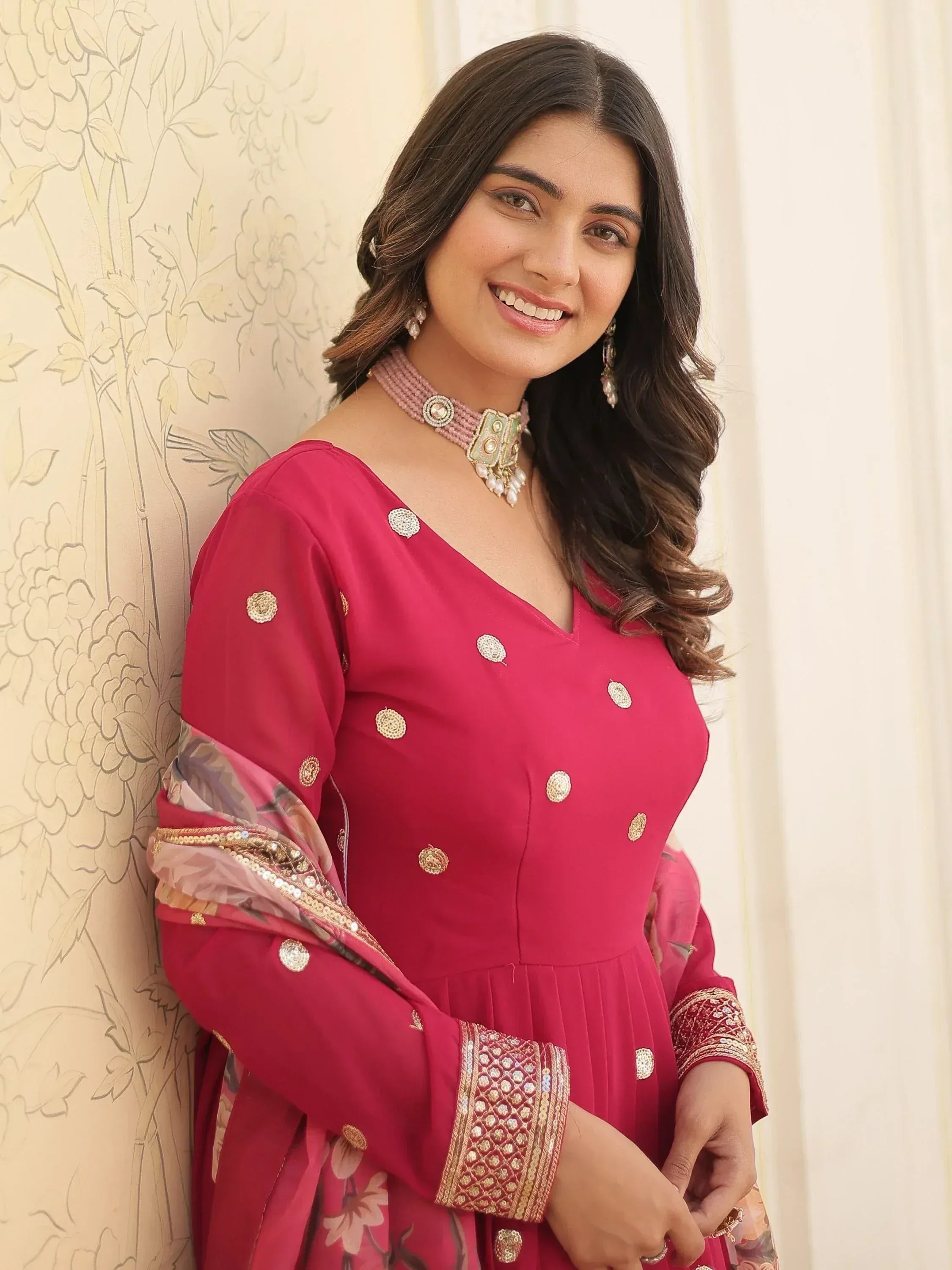 Woman in pink ethnic gown with gold embroidery and floral sleeves, styled with traditional jewelry