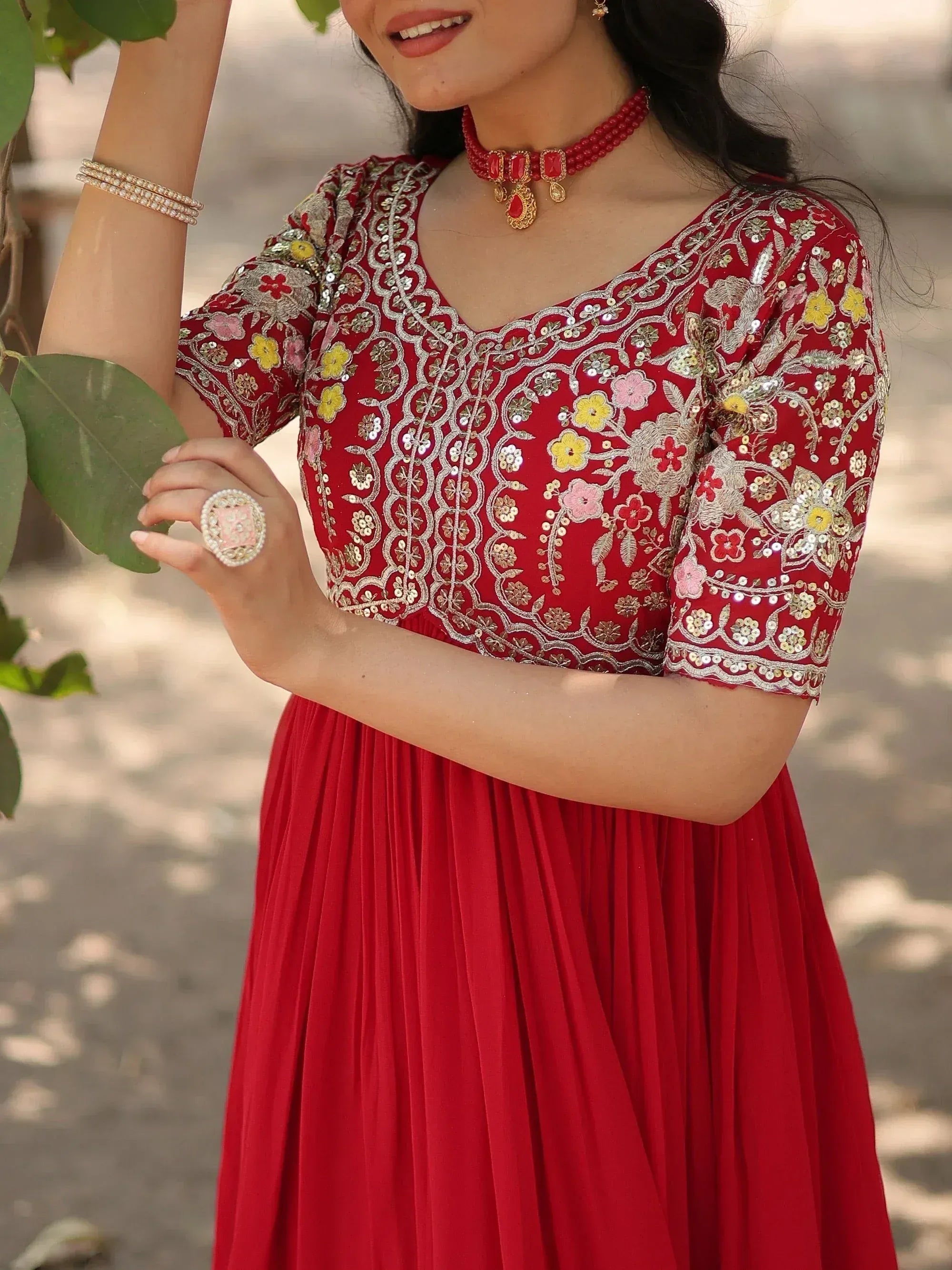 Red ethnic gown with floral embroidery and sequins, paired with traditional jewelry for festive occasions