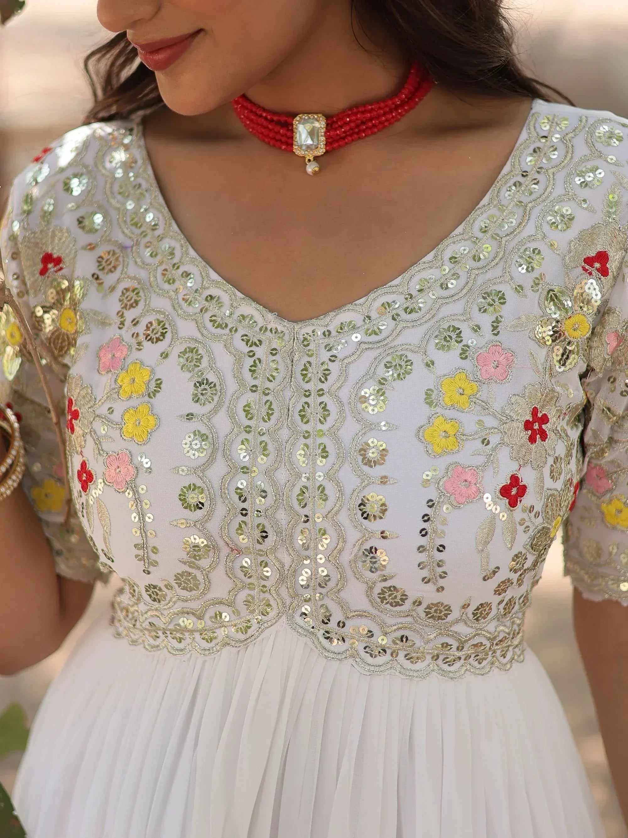 White ethnic gown with floral embroidery and sequins, paired with red beaded choker necklace
