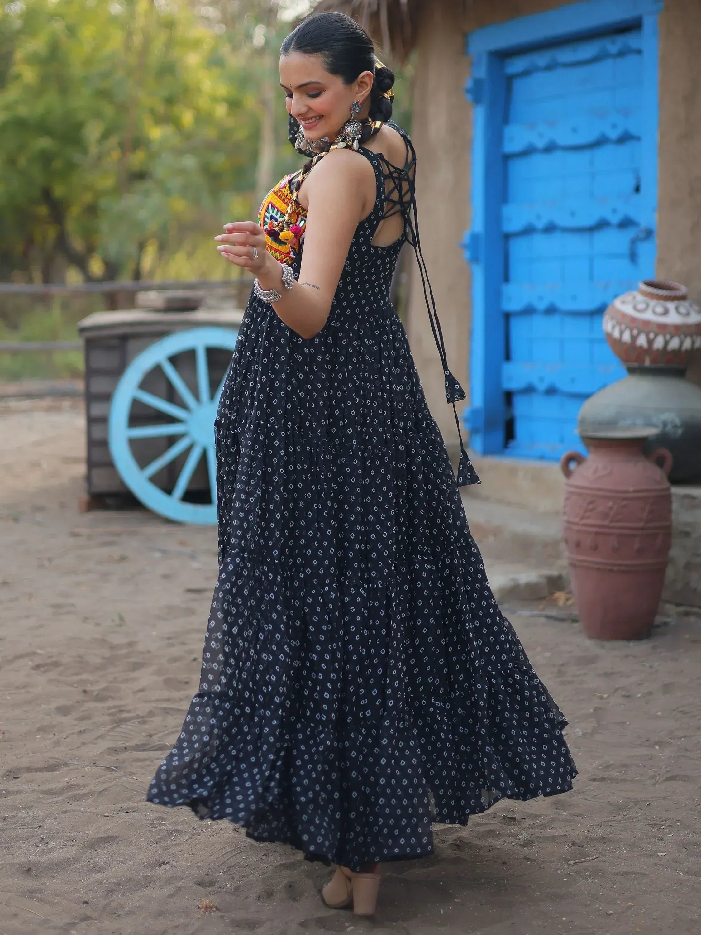 Woman in black printed ethnic gown with lace-up back, traditional jewelry, rustic village setting