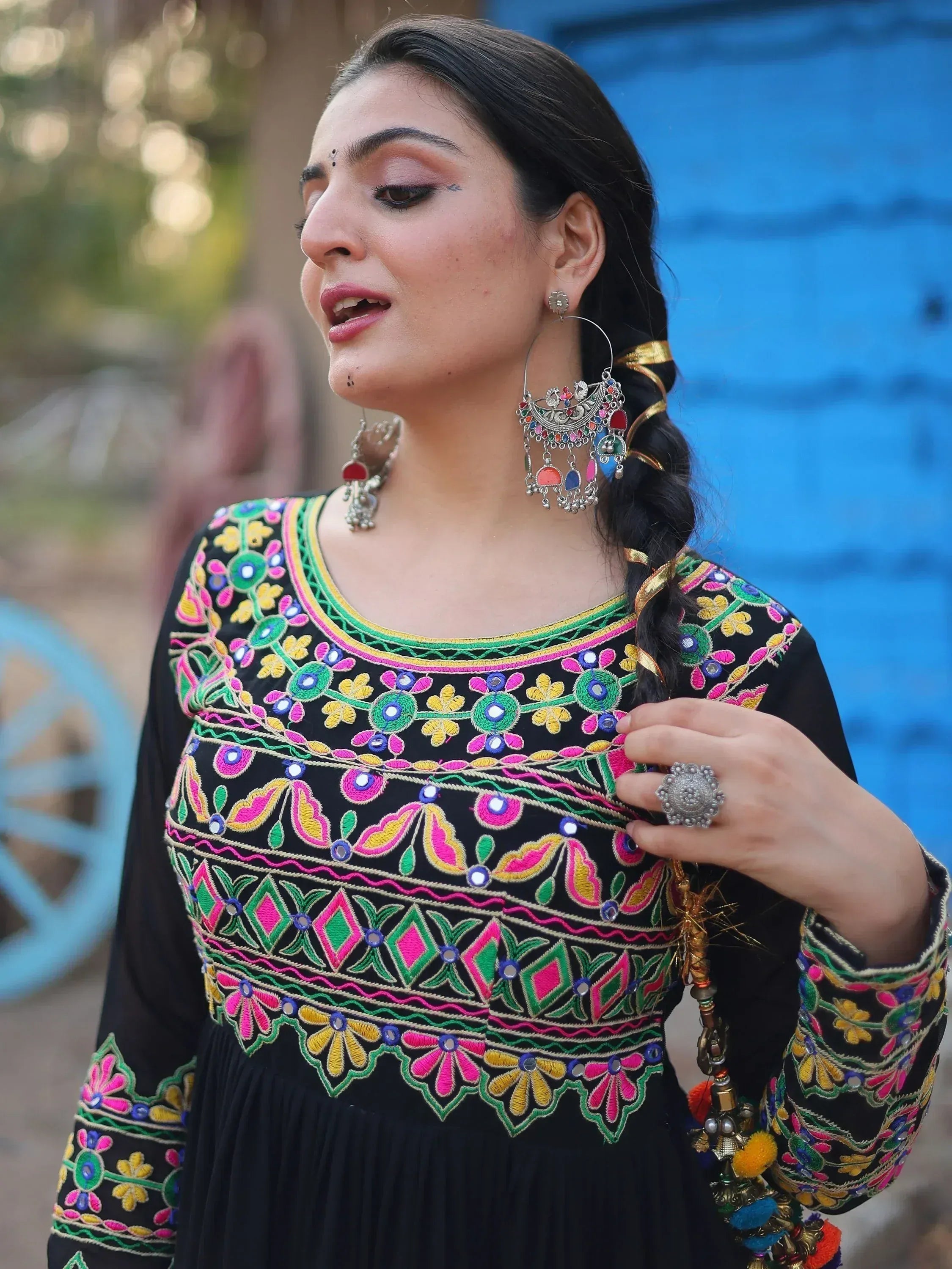 Woman in black embroidered ethnic gown with colorful mirror work, traditional jewelry, and braided hair