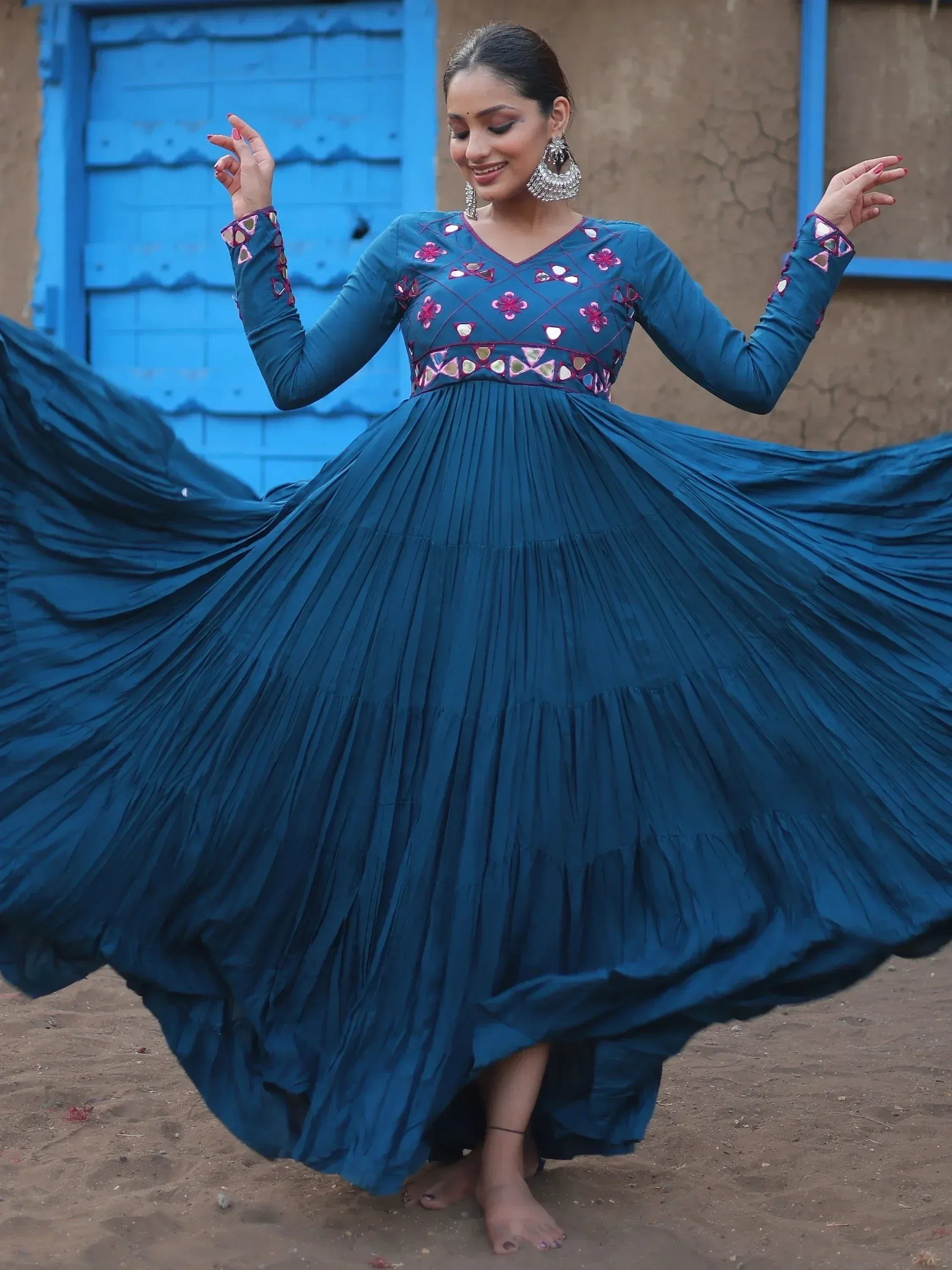 Woman twirling in teal ethnic gown with mirror work, perfect for Indian festive occasions.