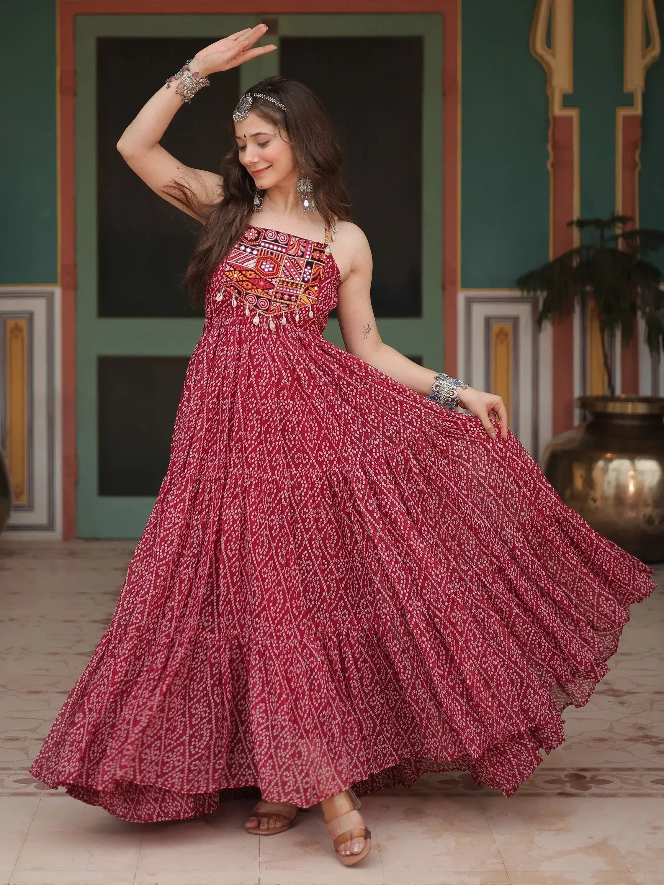 Woman in maroon ethnic gown with mirror work, dancing in traditional Indian setting