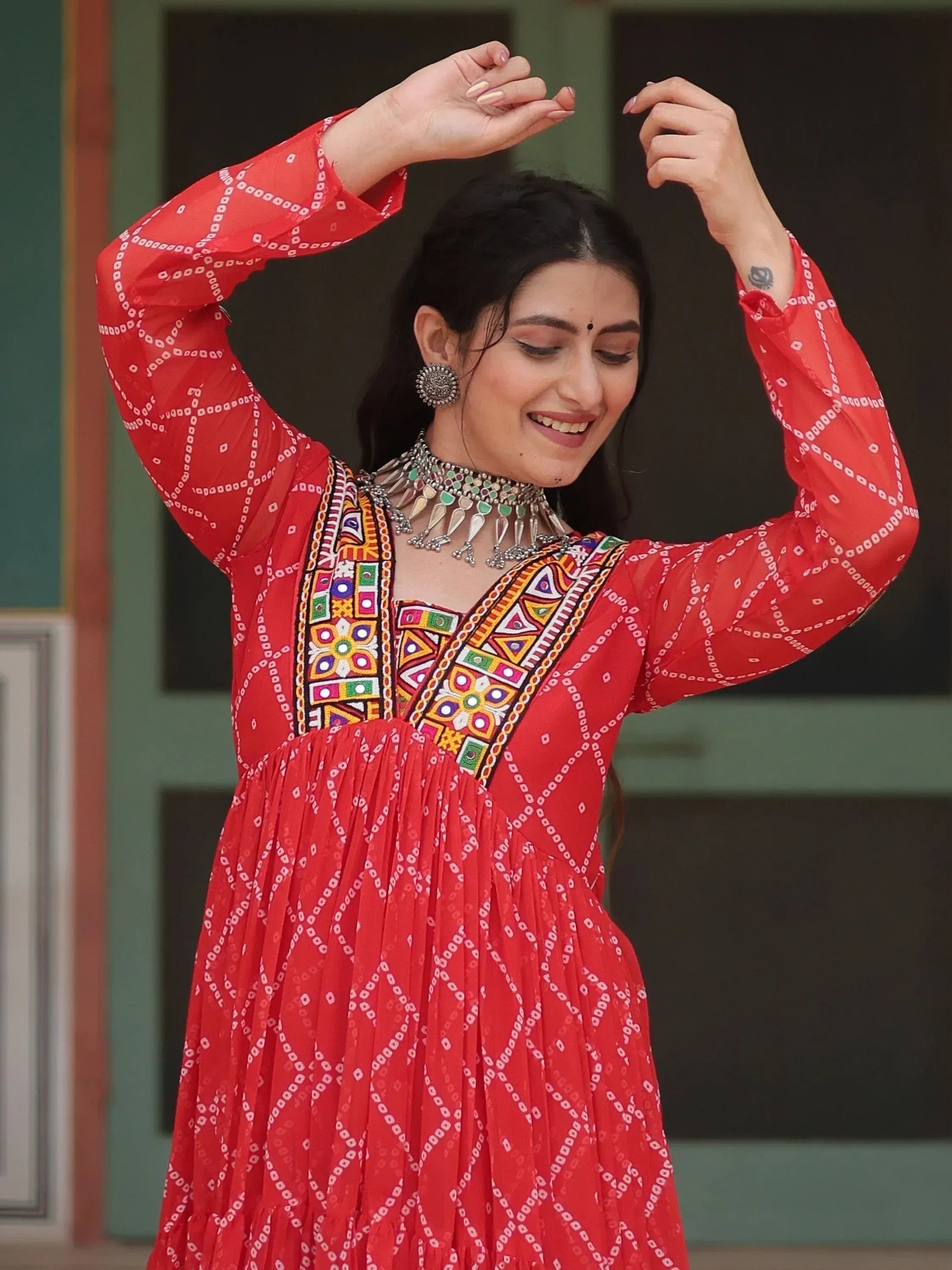 Woman in red ethnic gown with mirror work, dancing gracefully in traditional Indian attire.