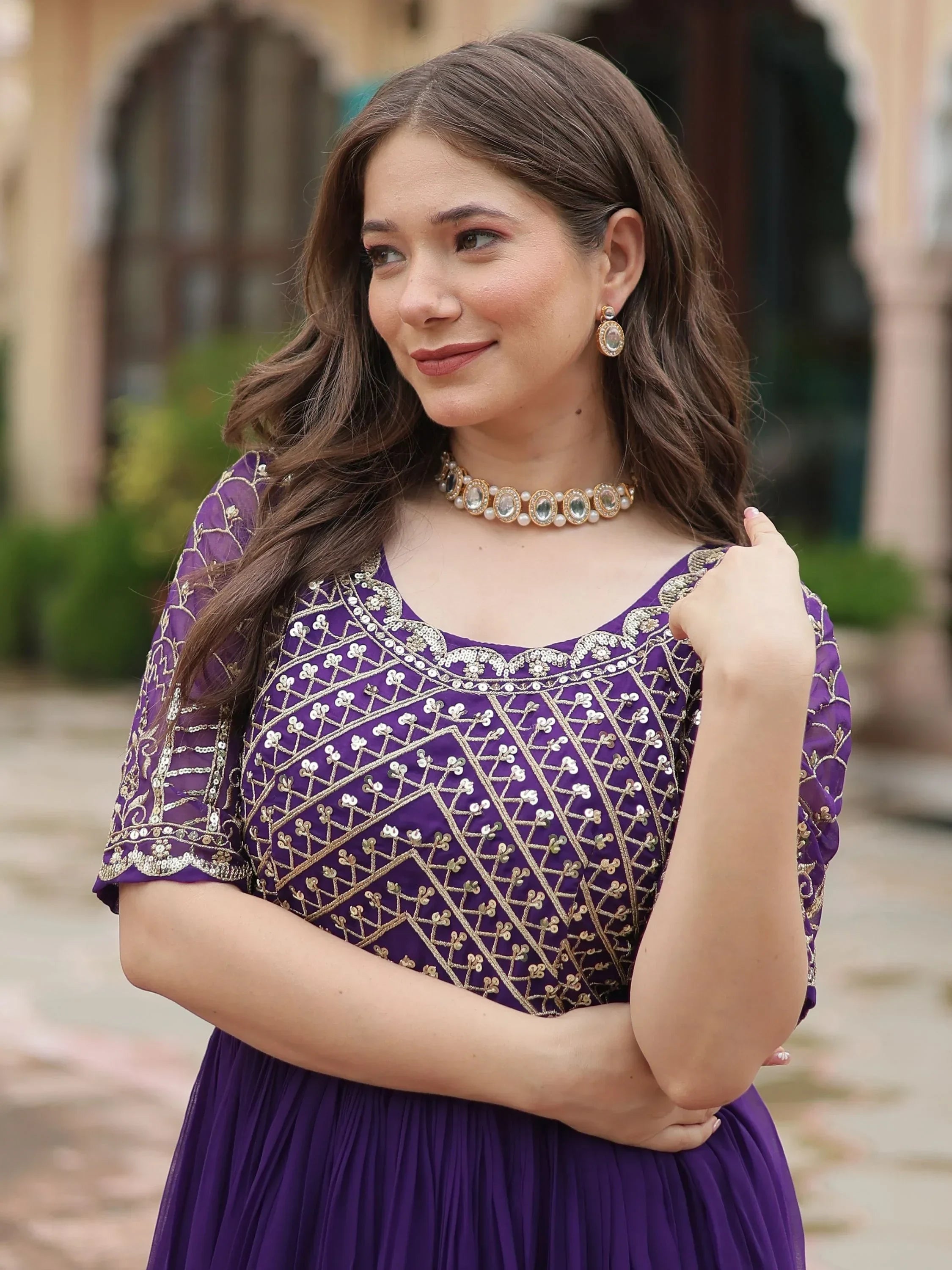 Woman in purple embroidered Indian ethnic gown with gold jewelry, outdoor setting