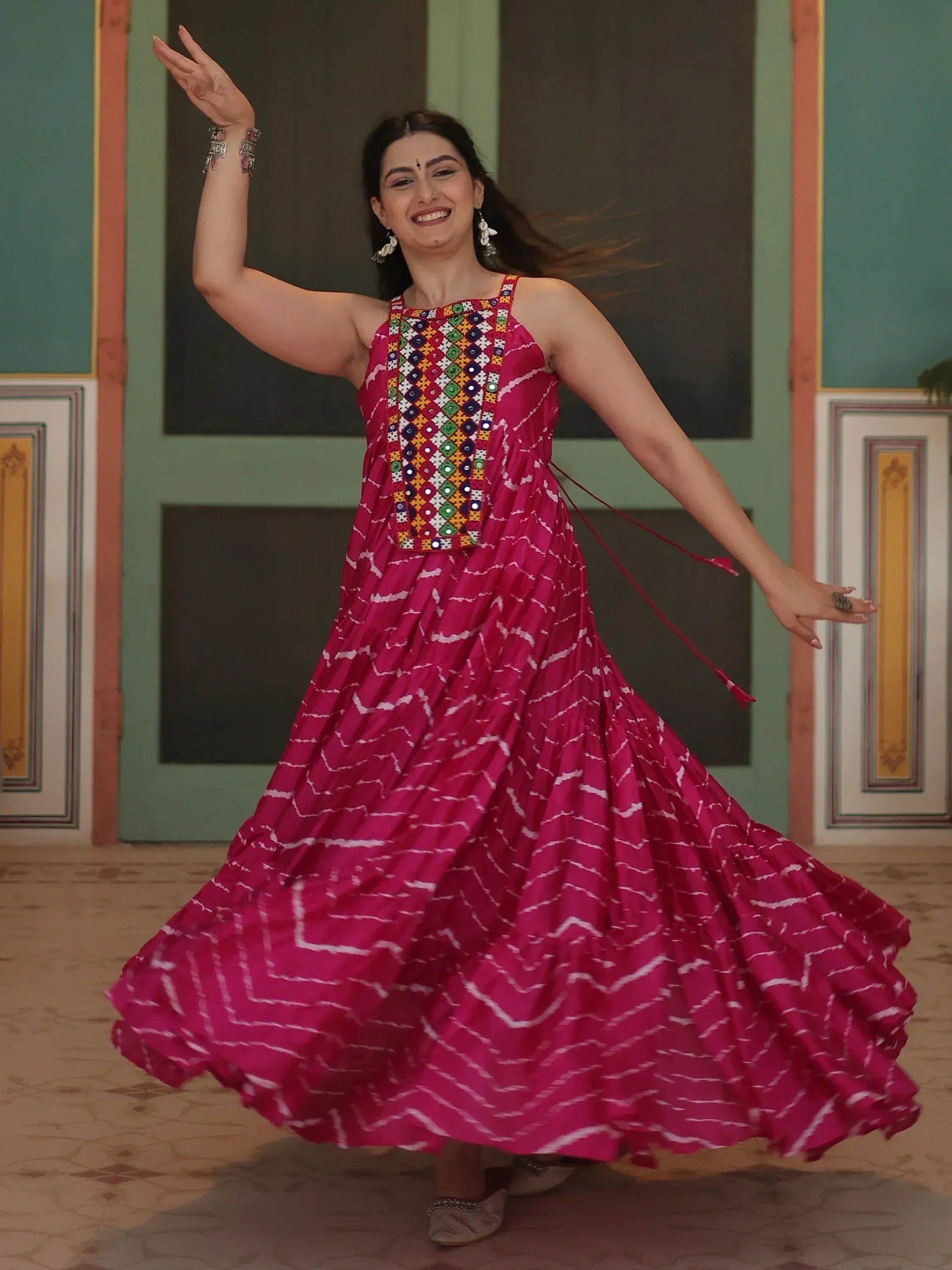 Woman twirling in vibrant pink ethnic gown with mirror work and pleated skirt, perfect for festive occasions.