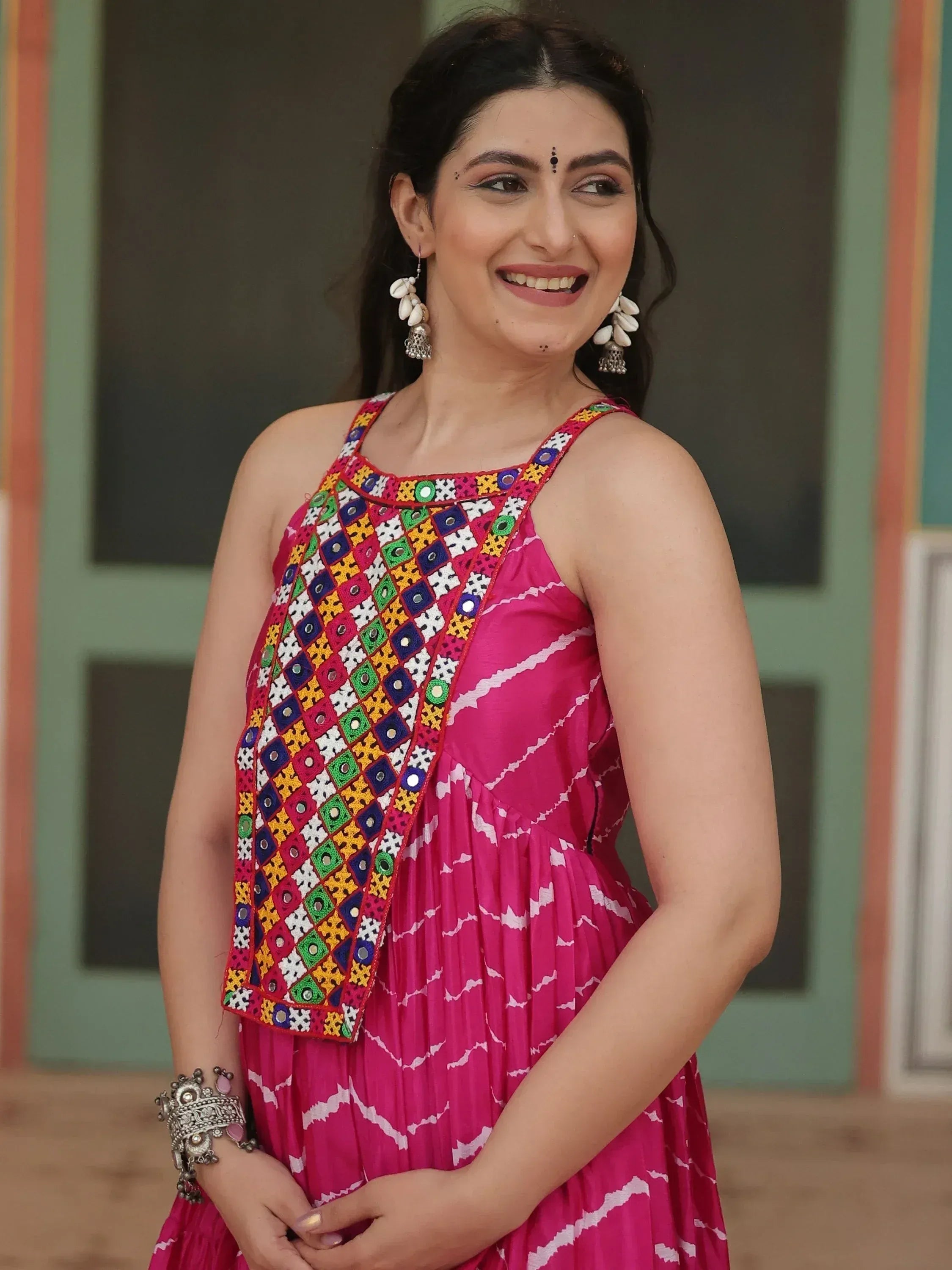 Pink ethnic gown with colorful mirror work and white patterns, paired with traditional jewelry