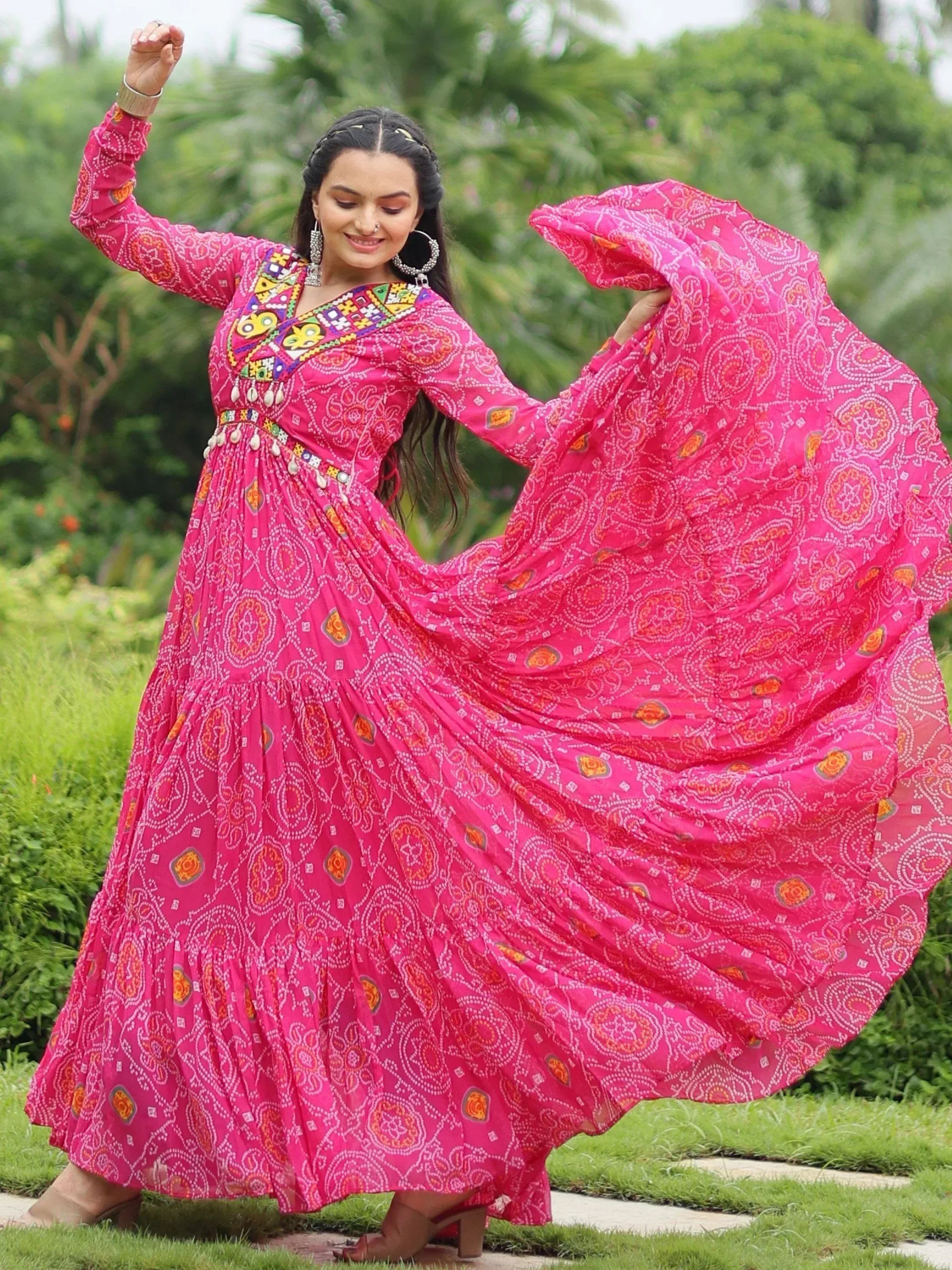 Woman in vibrant pink ethnic gown with mirror work, twirling outdoors in garden setting