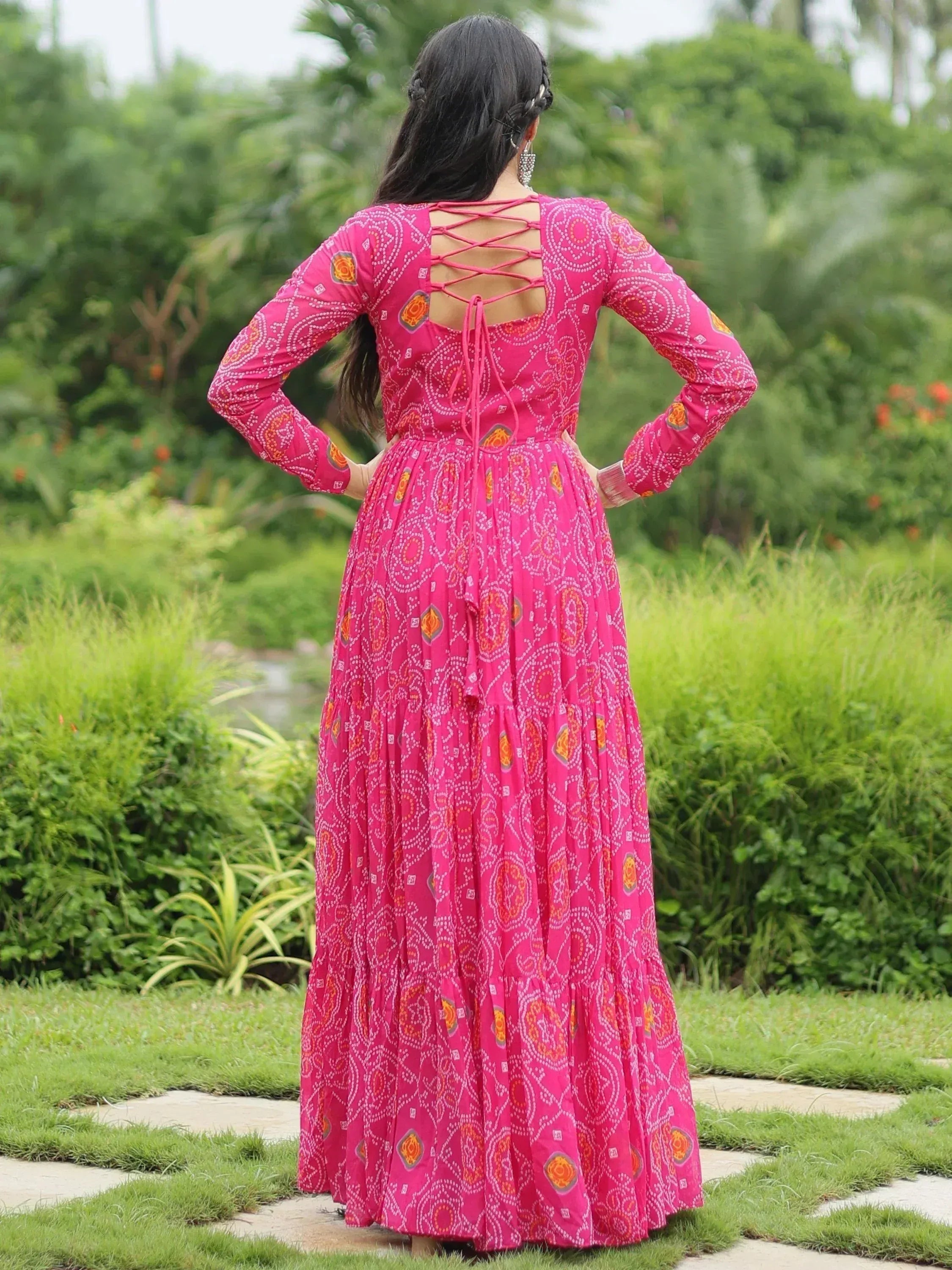 Pink ethnic gown with crisscross back, long sleeves, and printed patterns, worn in a garden setting