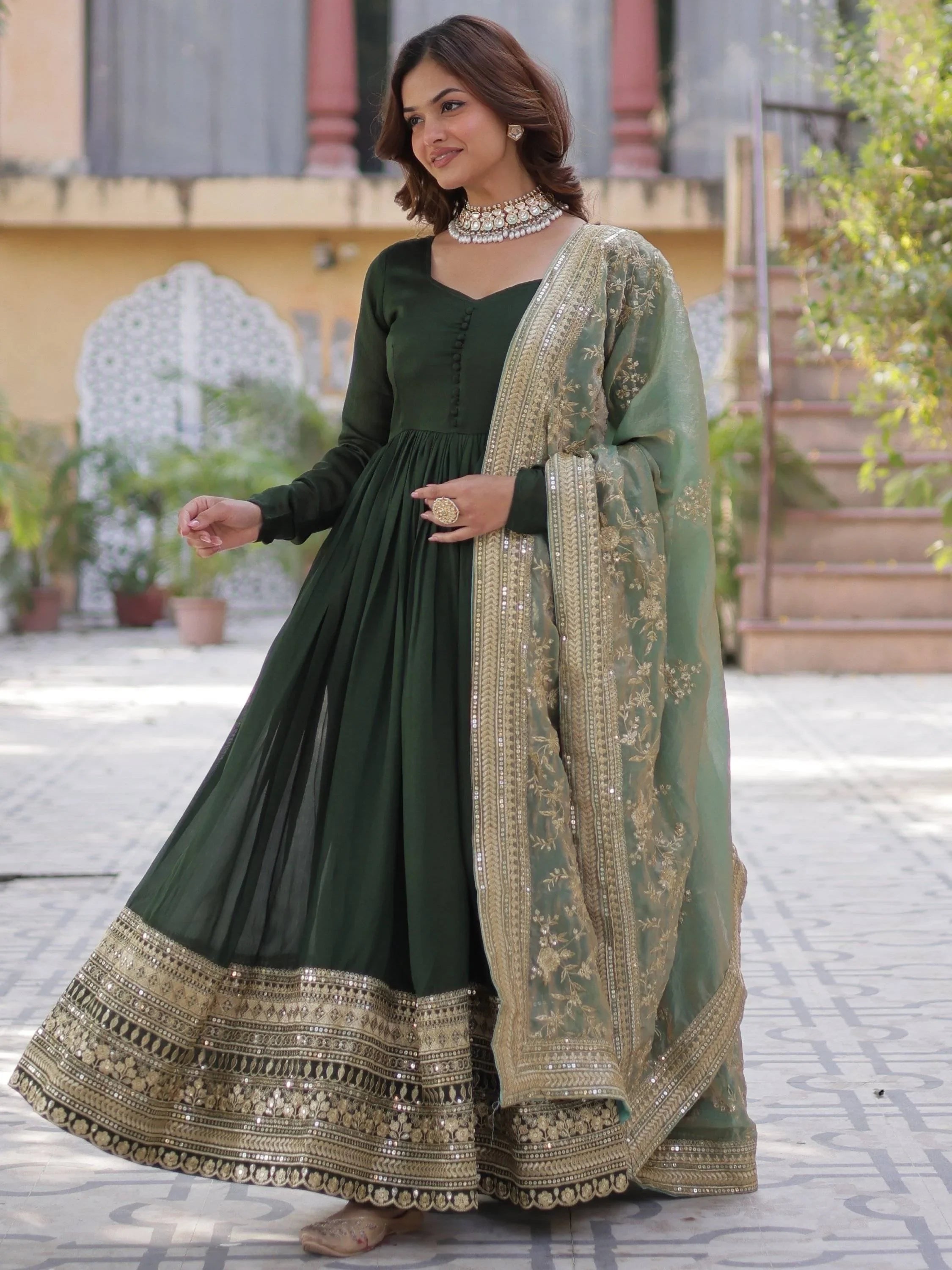 Woman in green embroidered Indian ethnic gown with gold dupatta, wearing jewelry outdoors