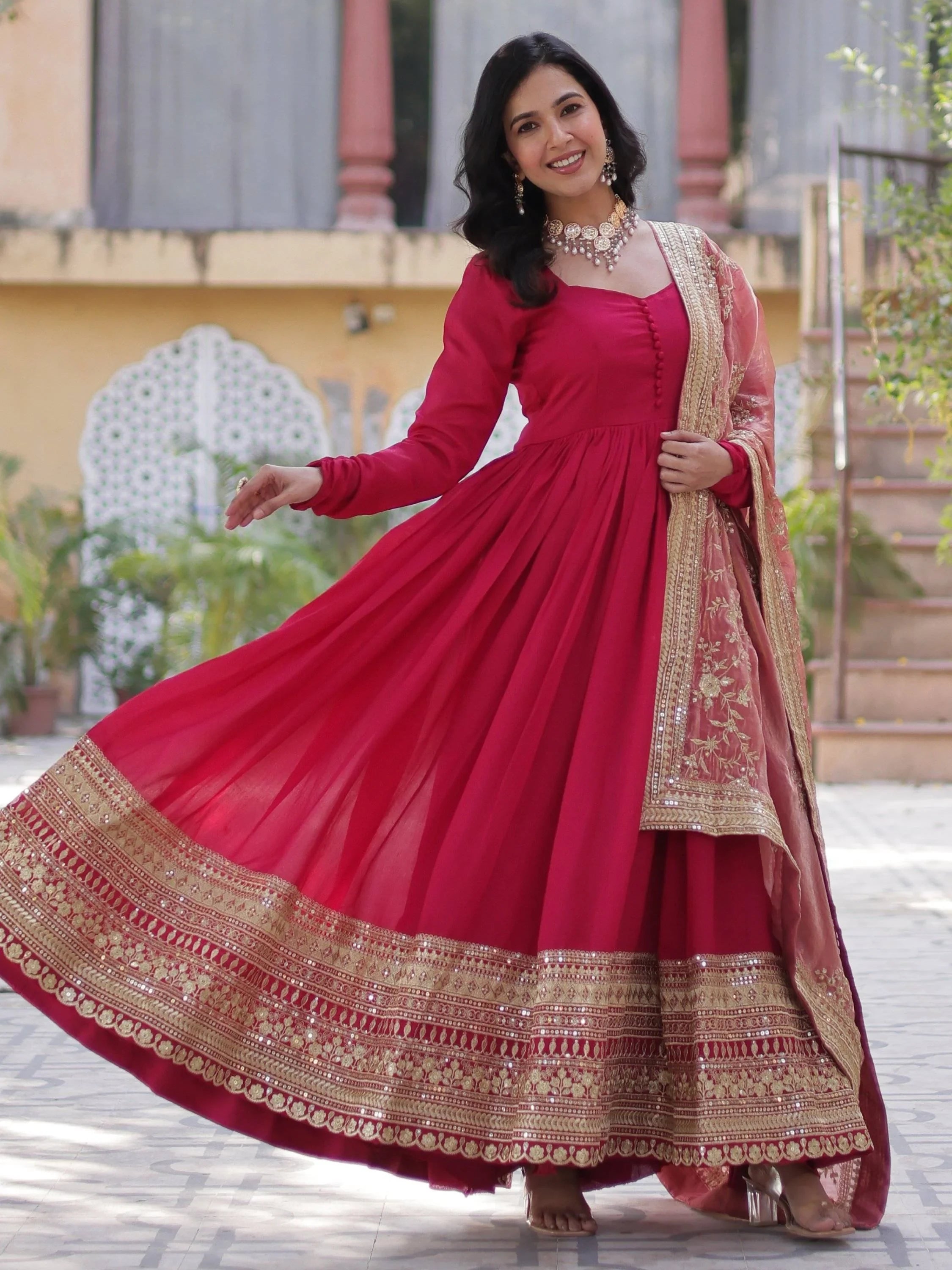 Woman in pink ethnic gown with gold embroidery, wearing traditional jewelry outdoors