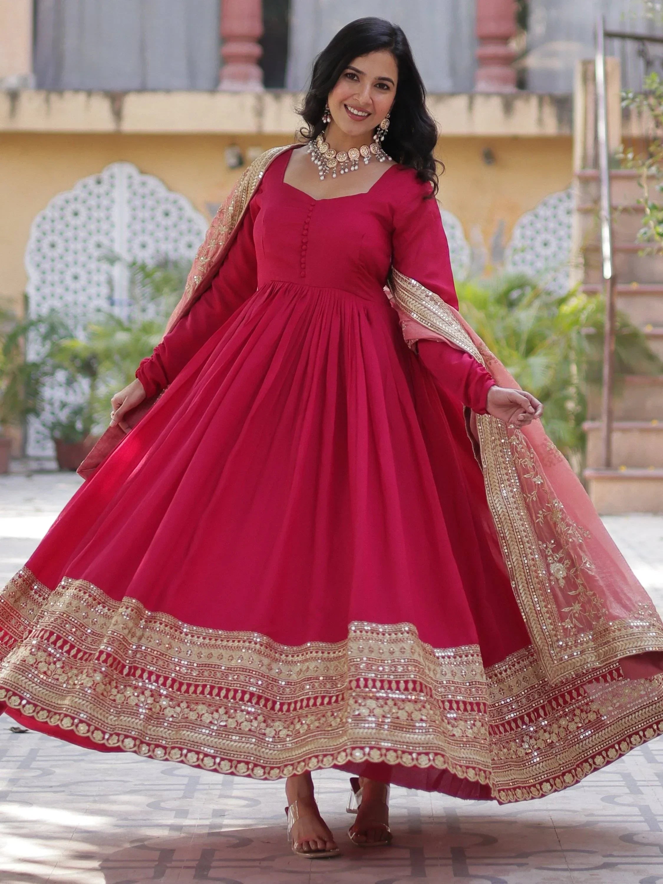 Woman wearing pink ethnic gown with gold embroidery border and matching dupatta, outdoor setting