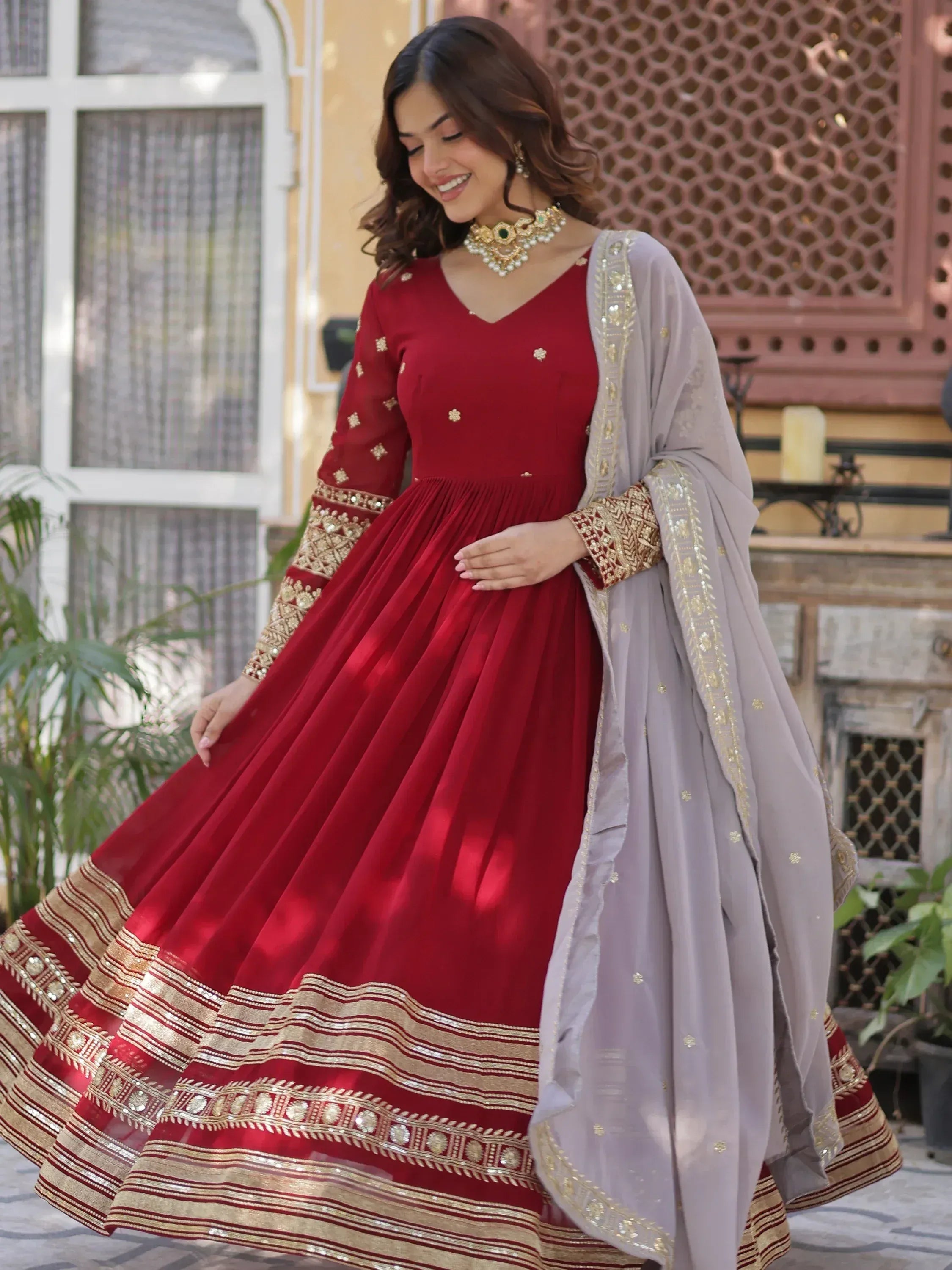 Woman in red embroidered Anarkali gown with gold detailing and light dupatta, Indian ethnic wear