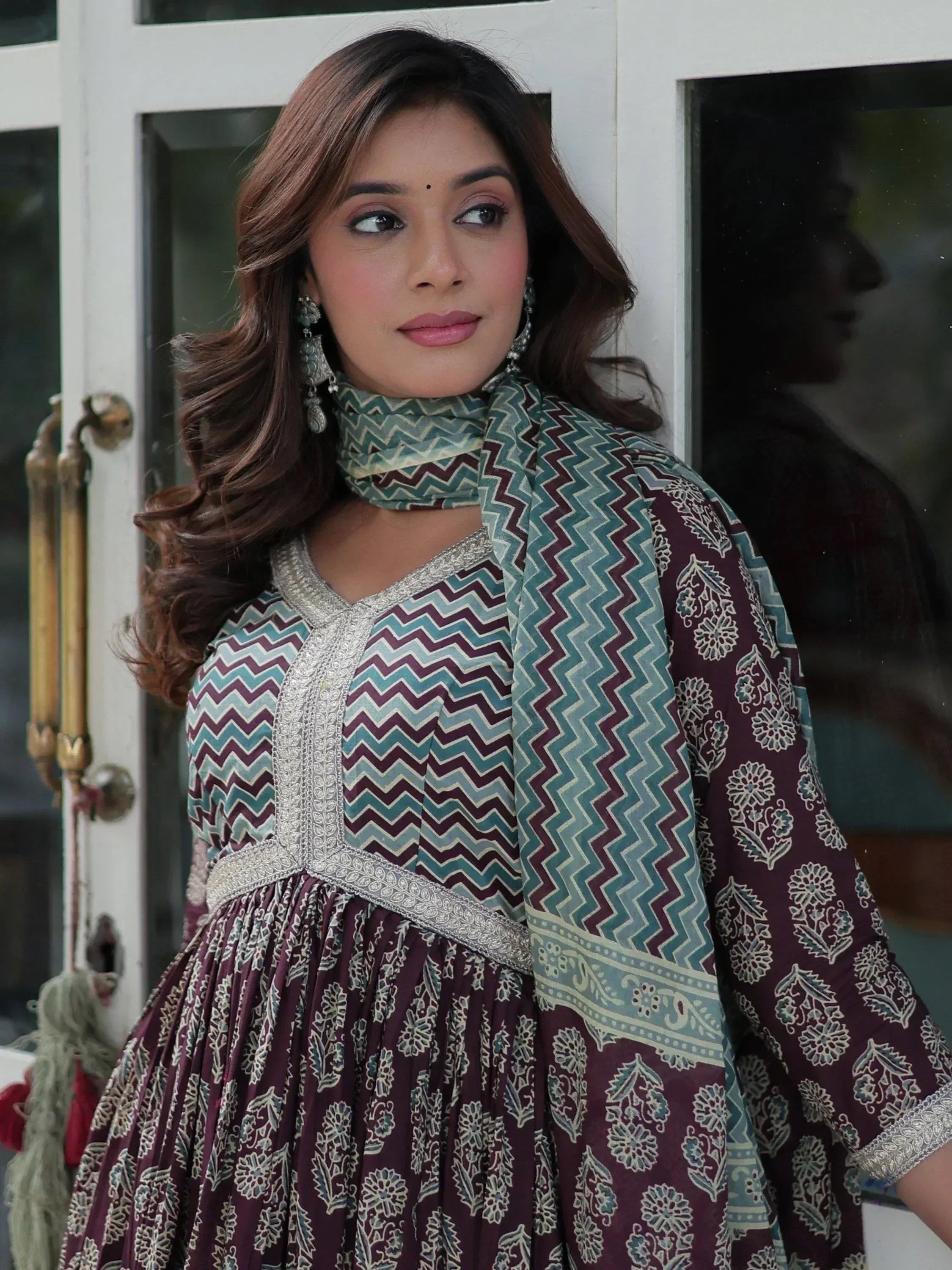 Woman in maroon and teal printed ethnic gown with silver embroidery, styled with matching dupatta and jhumka earrings