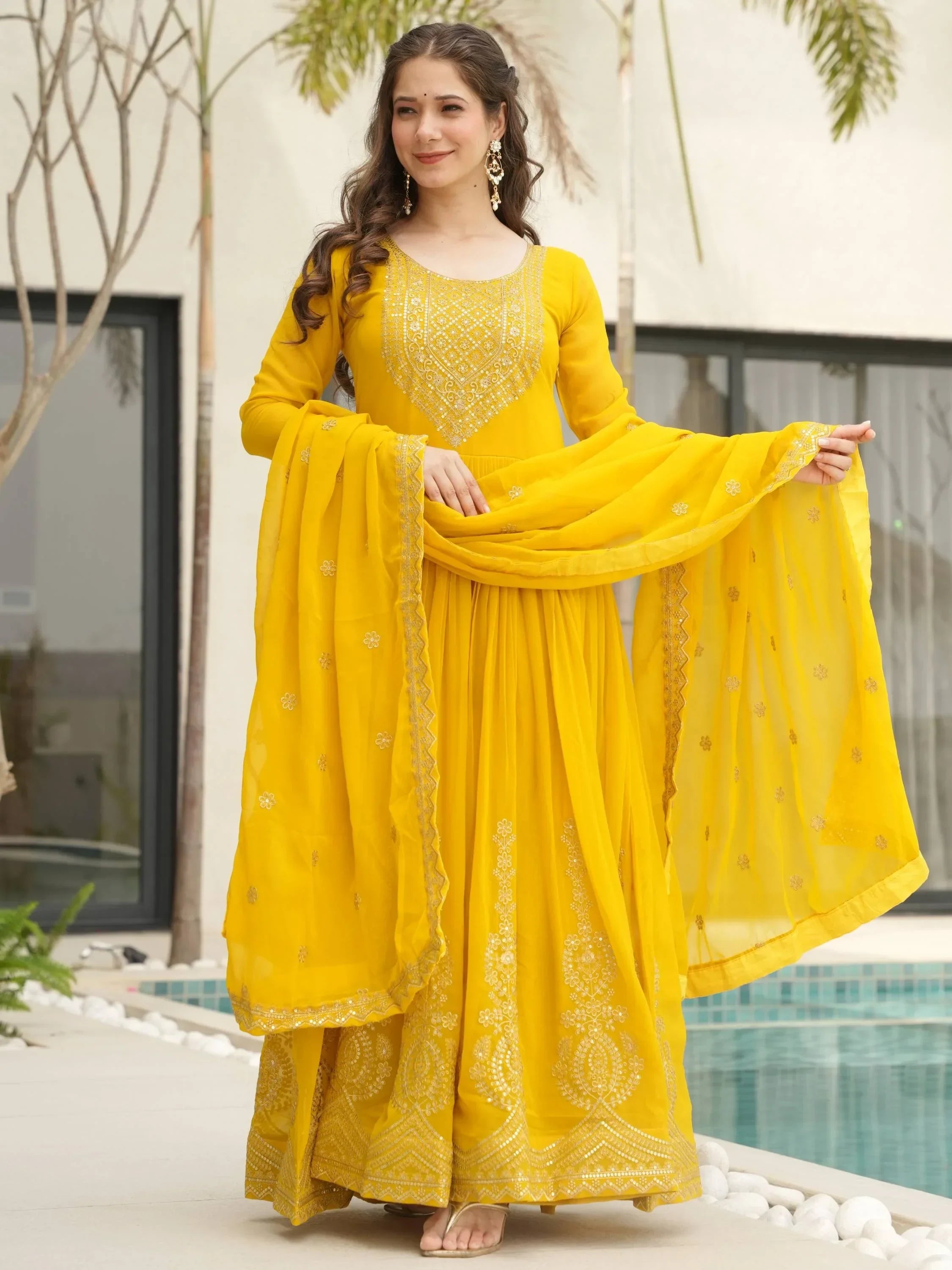 Woman wearing yellow embroidered designer Anarkali suit with dupatta by poolside