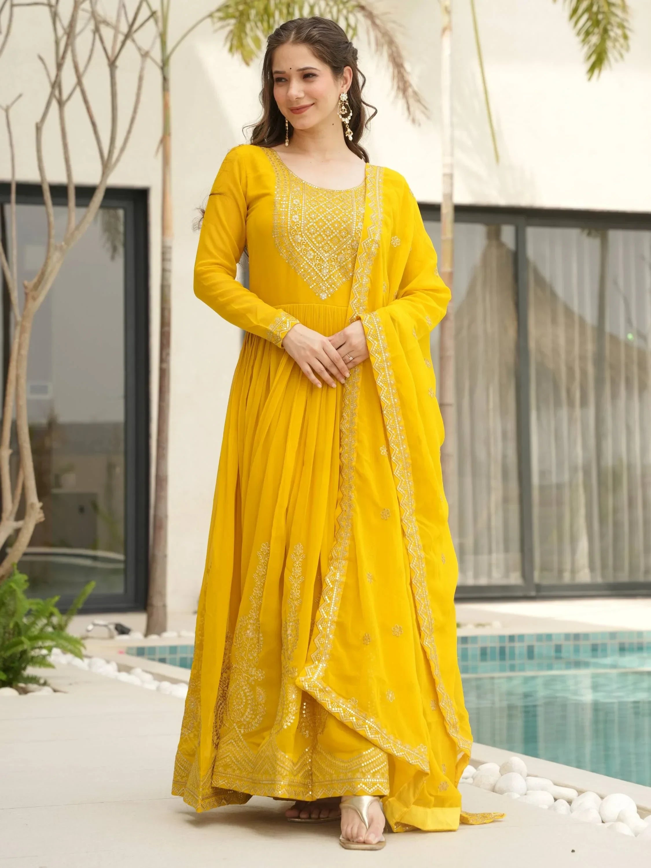 Woman in yellow embroidered Anarkali suit with matching dupatta by a poolside