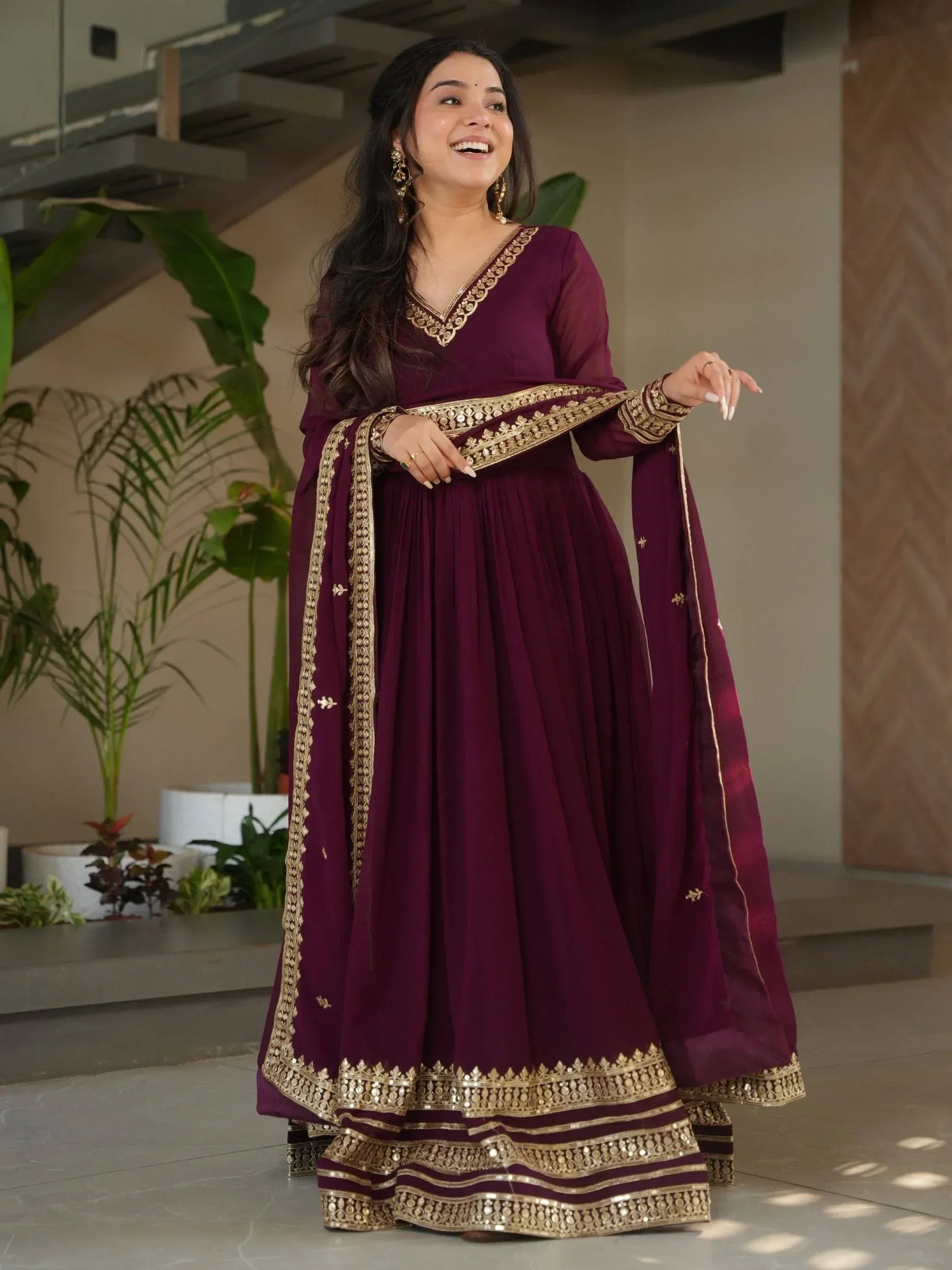 Woman in maroon ethnic gown with gold embroidery, perfect for Indian occasions and festive wear.